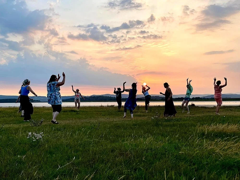 People dancing in a wide open space as the sun sets over the Lake District fells