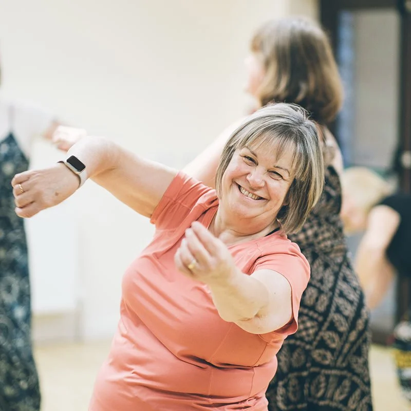 A joyful woman smiling and dancing with a group of friends on the dancefloor.