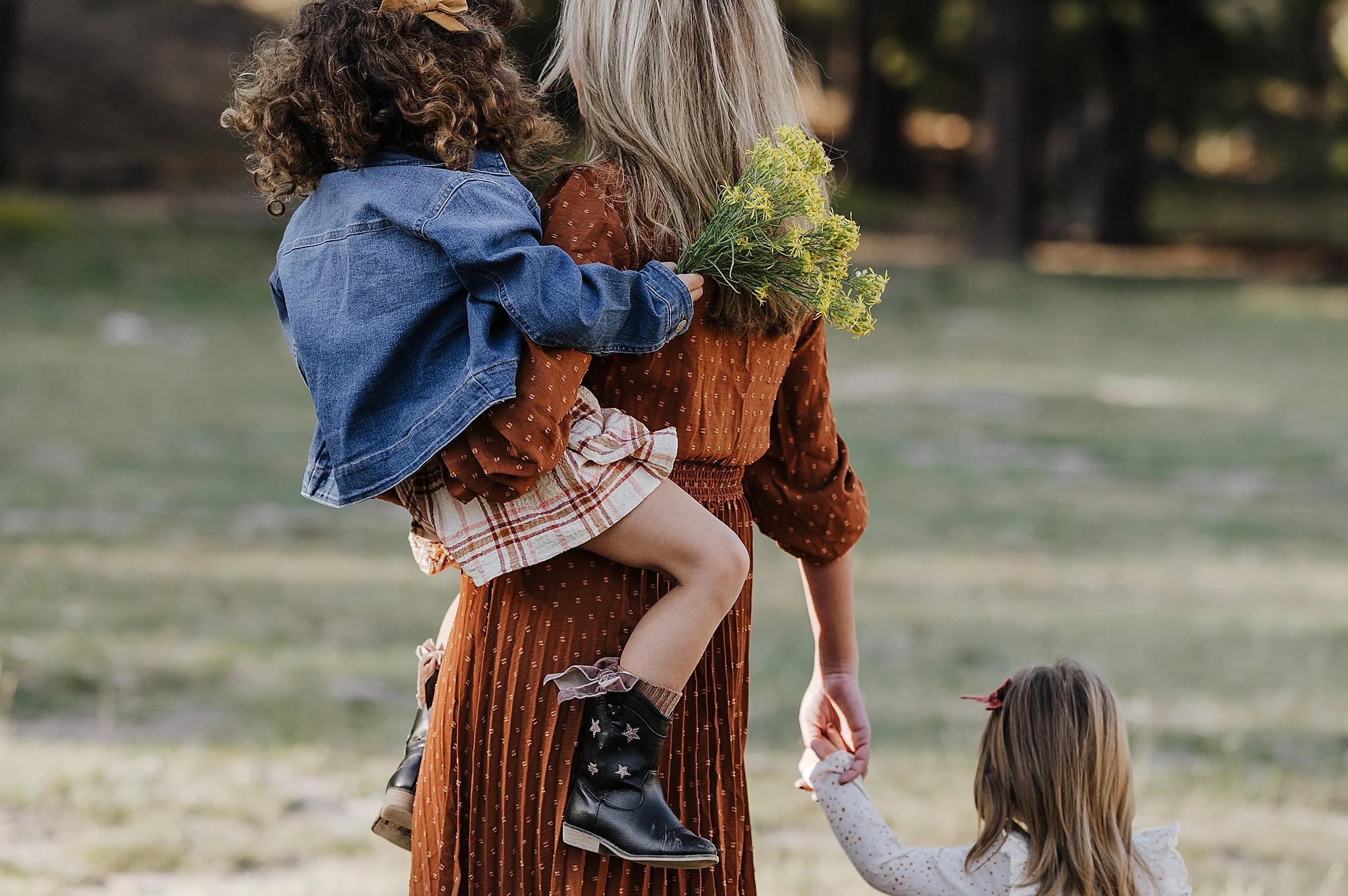 A mom in a burnt orange dress holding one daughter and holding the and of her other toddler daughter near Las Vegas.