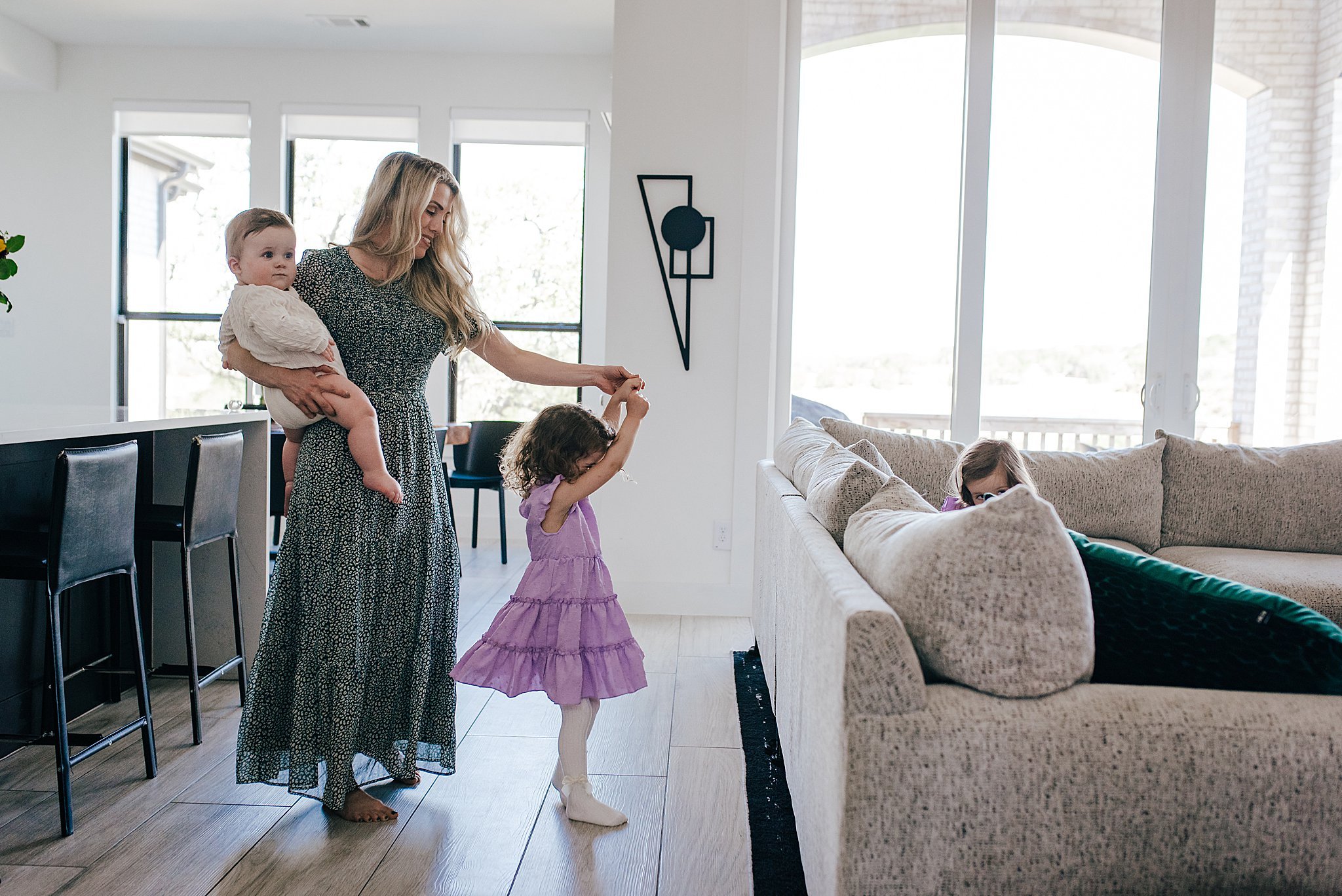 Mom in a modern interior design living room, twirling her toddler daughter, and holding baby son, taken on Nikon Z6ii.