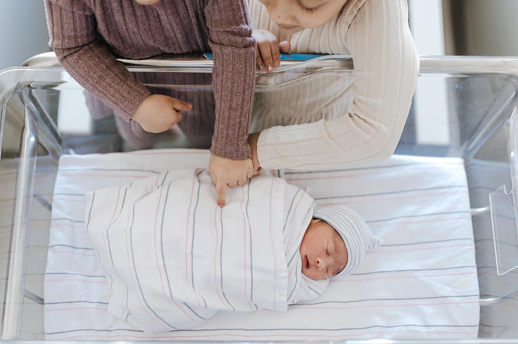 Newborn photography in a Las Vegas hospital with sisters looking on a newborn baby.