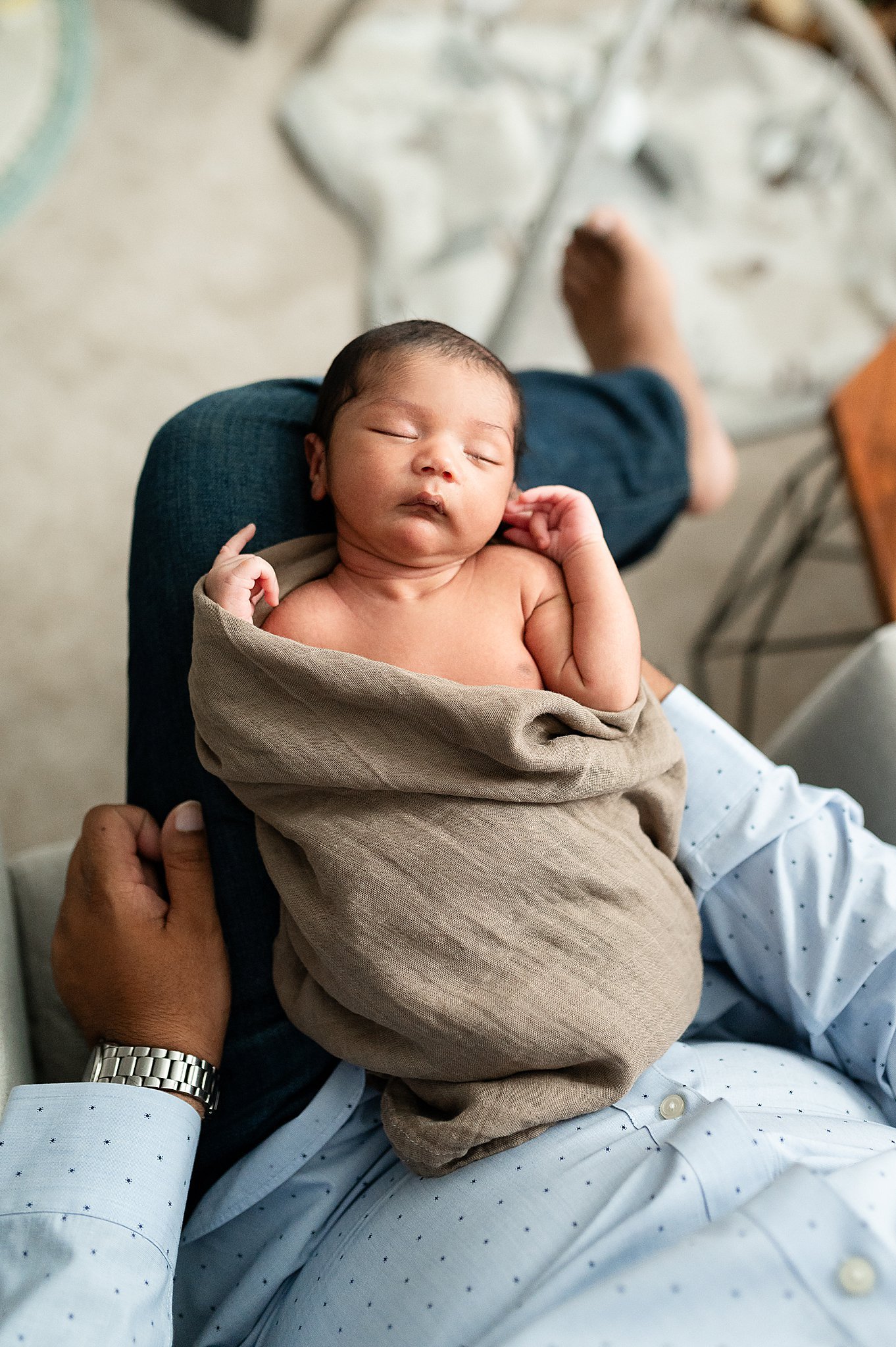 Sweet newborn, in a loose swaddle, sleeping on his dad's lap, taken by Alyssa Charboneau Photography.