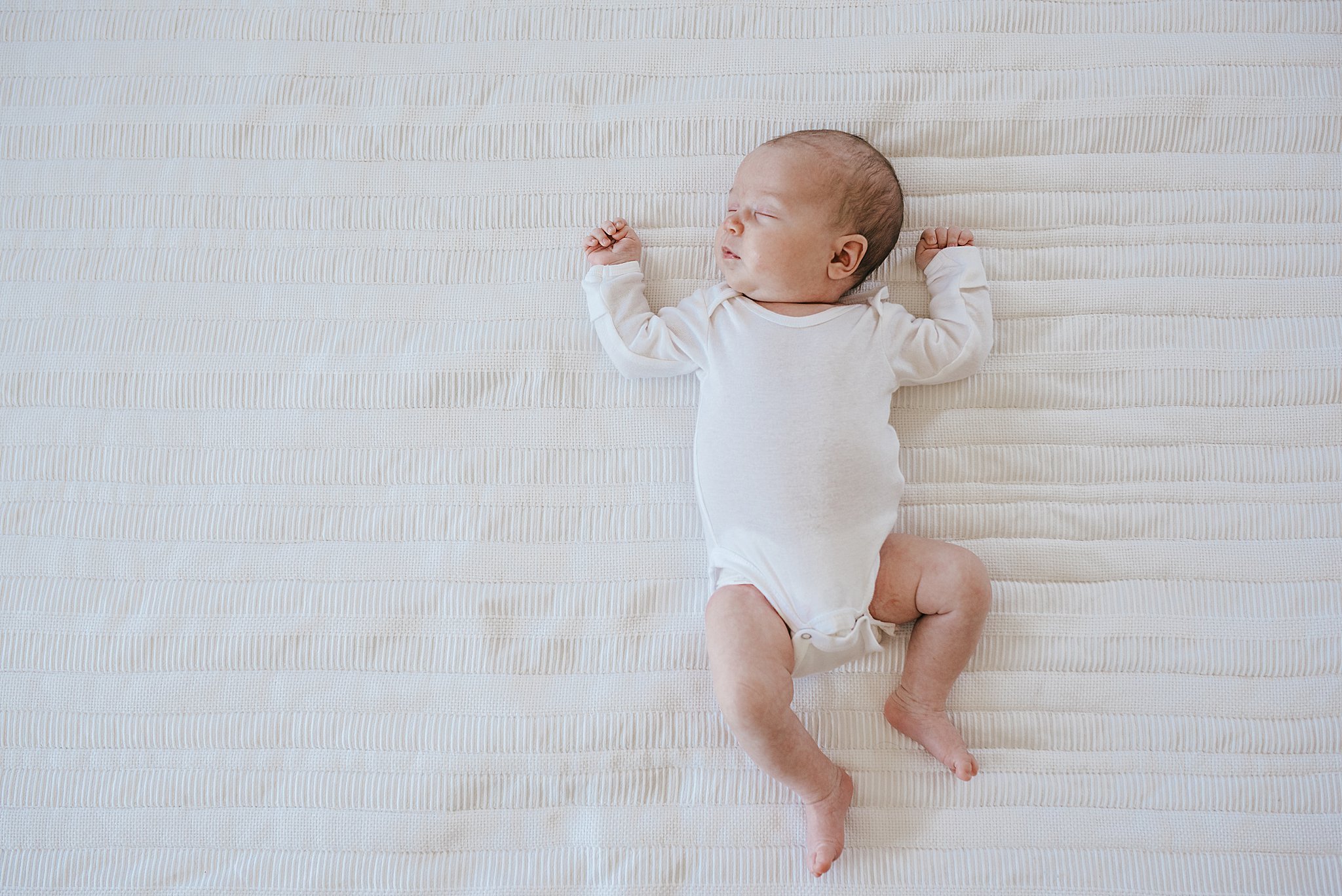Newborn baby sleeping on a white bed, in an in-home newborn session in Las Vegas, NV.