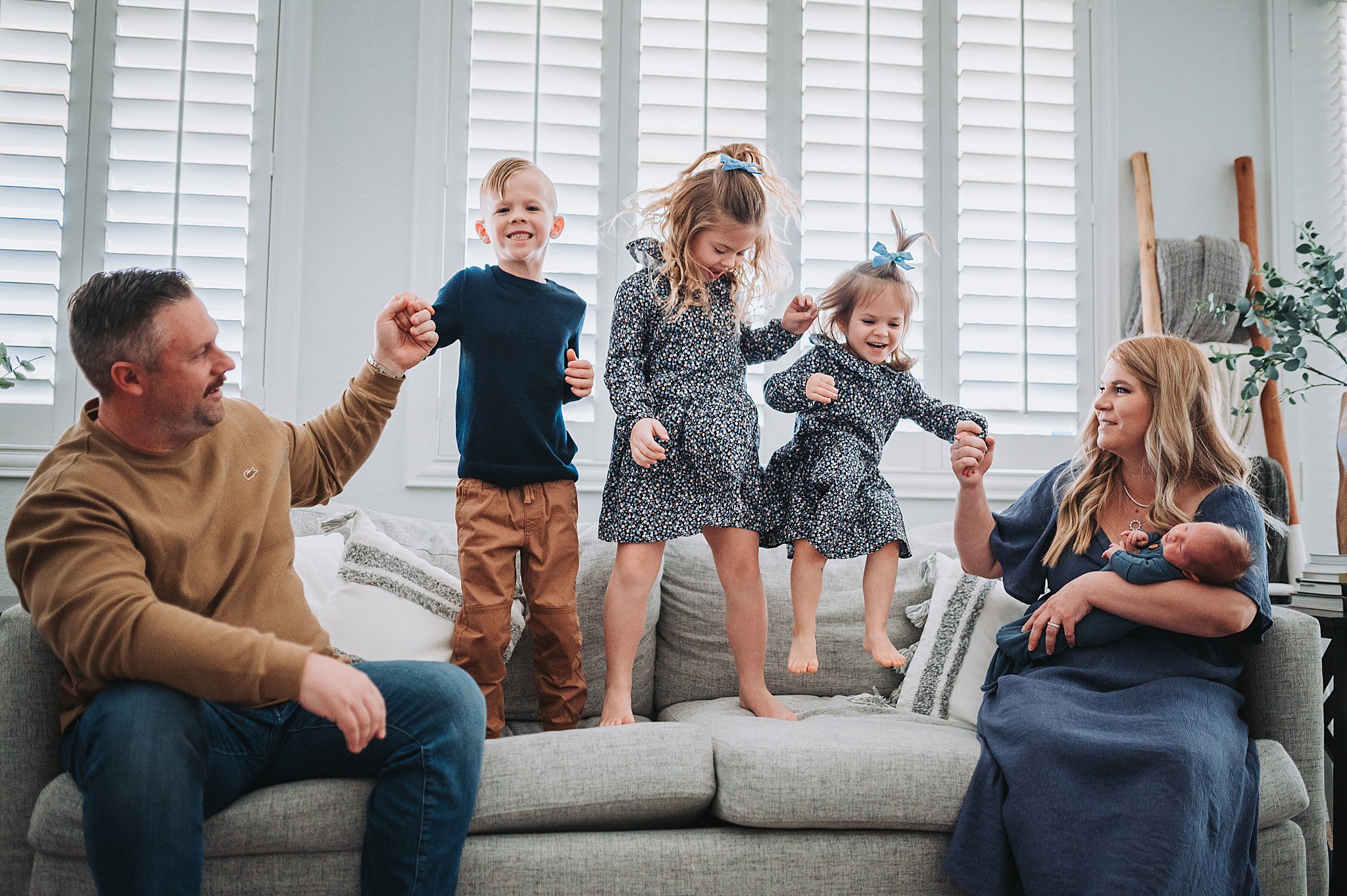 A family of six, with toddlers jumping on the couch and mom holding a newborn baby, in Vistas, Summerlin, Las Vegas.