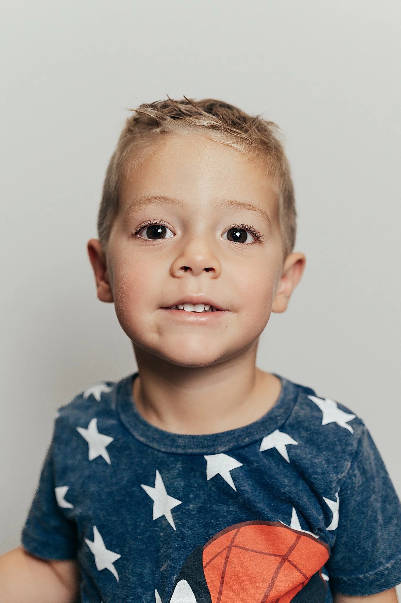 Preschool boy in a Spiderman shirt smiling for his class photo.