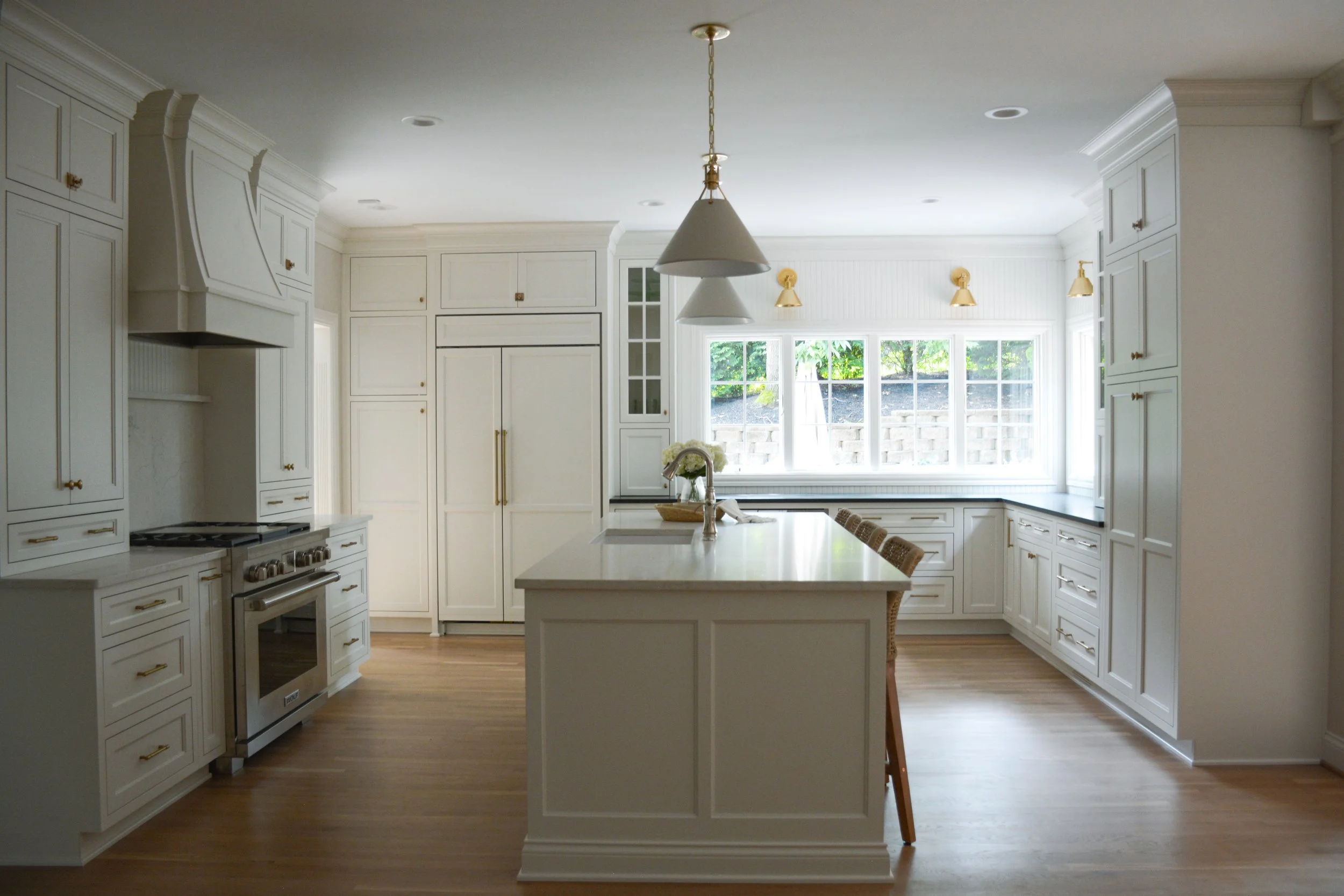 A timeless kitchen design by Studio Nine Interiors featuring built-in cabinetry, gold finishes, and a bright, inviting layout anchored by a central island.