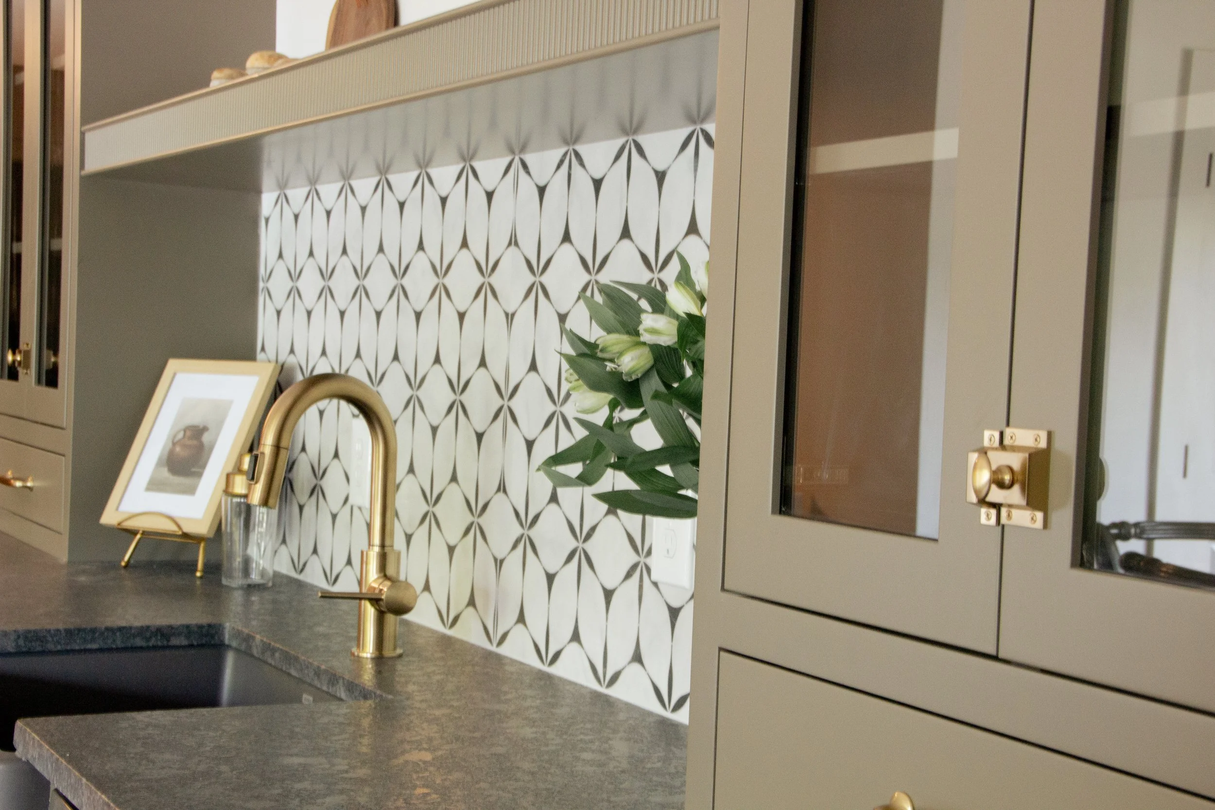 Custom beverage station featuring a geometric tile backsplash, brass faucet, dark stone countertop, and built-in cabinetry designed as part of a full-scale home renovation.
