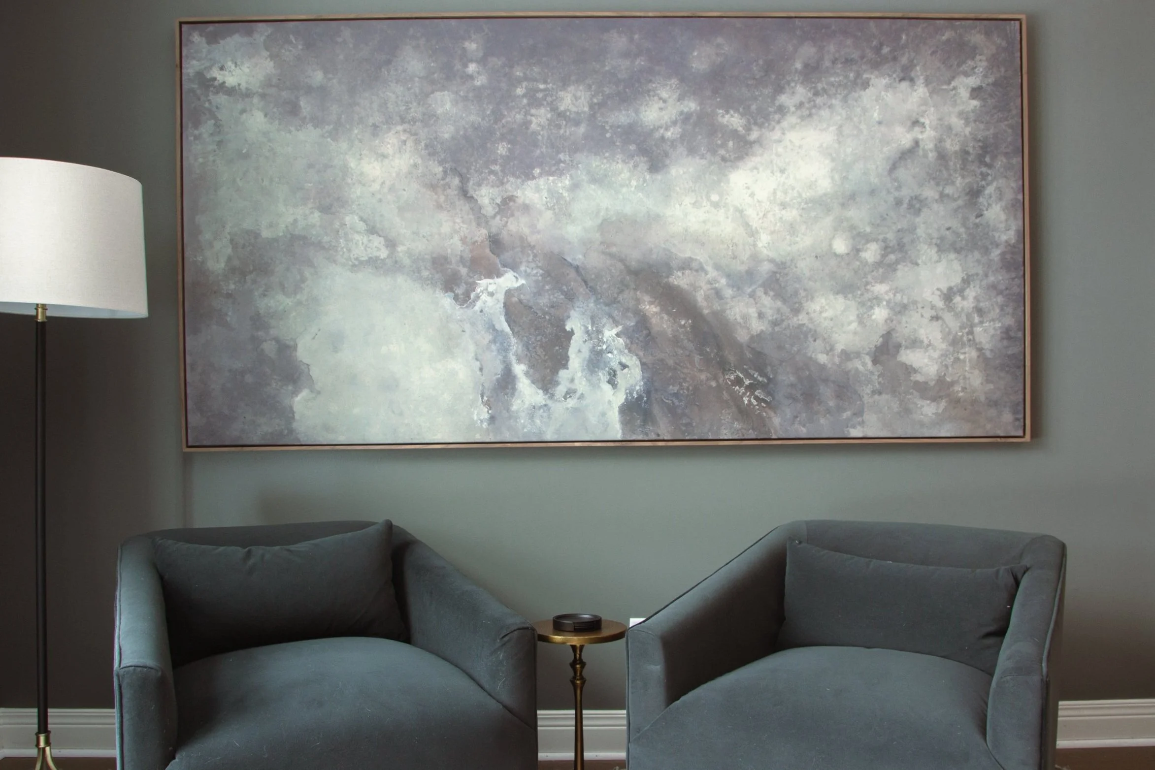 Two upholstered accent chairs beneath oversized abstract artwork in a thoughtfully designed sitting area with layered neutral tones.