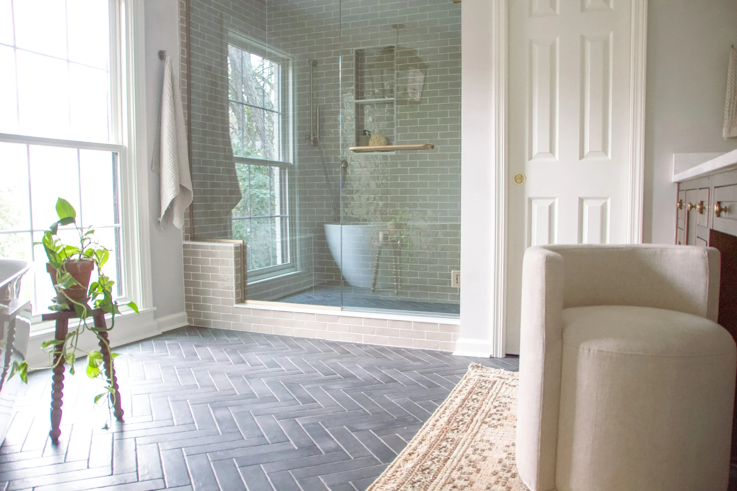 Glass-enclosed shower with soft green tile, herringbone stone flooring, and natural light creating an open, spa-inspired layout.