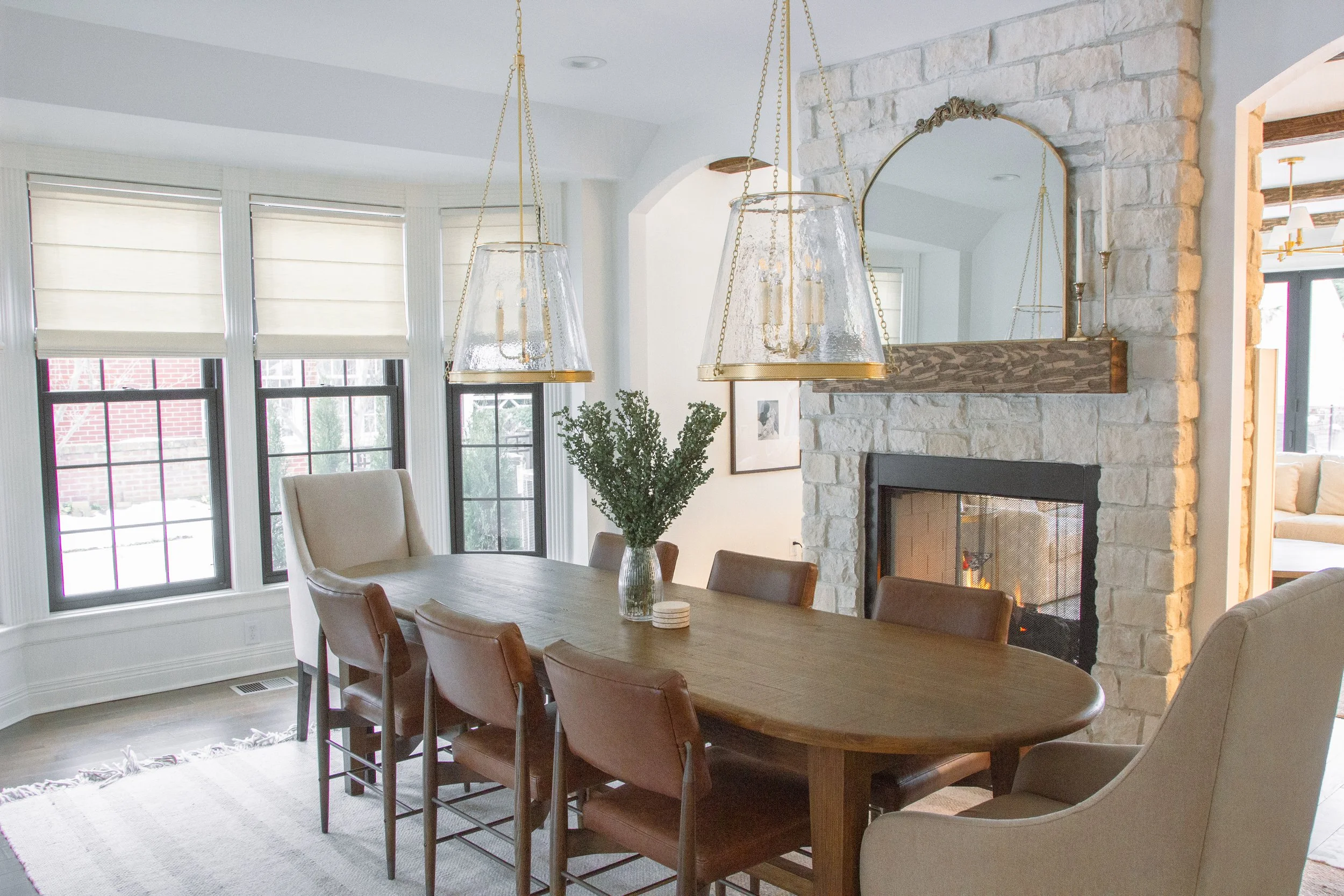 Dining room featuring a wood dining table, leather seating, a stone fireplace, and statement pendant lighting in a transitional interior.
