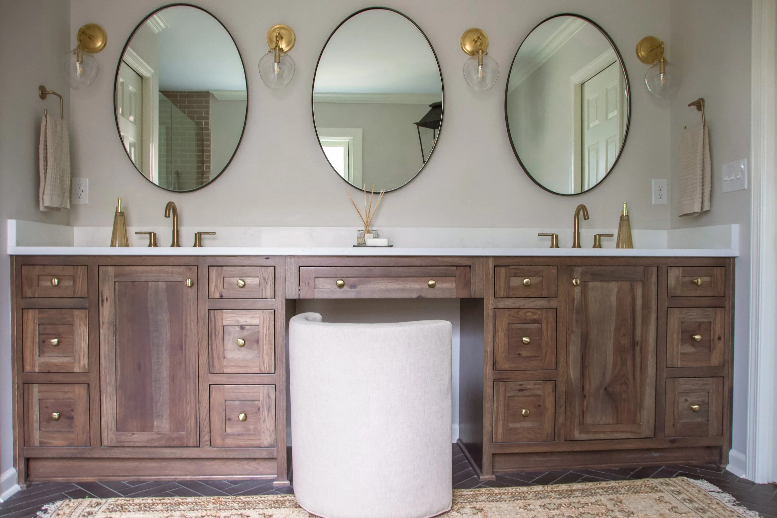 Wood double vanity with integrated storage, brass hardware, oval mirrors, and balanced lighting arranged with symmetry and restraint.