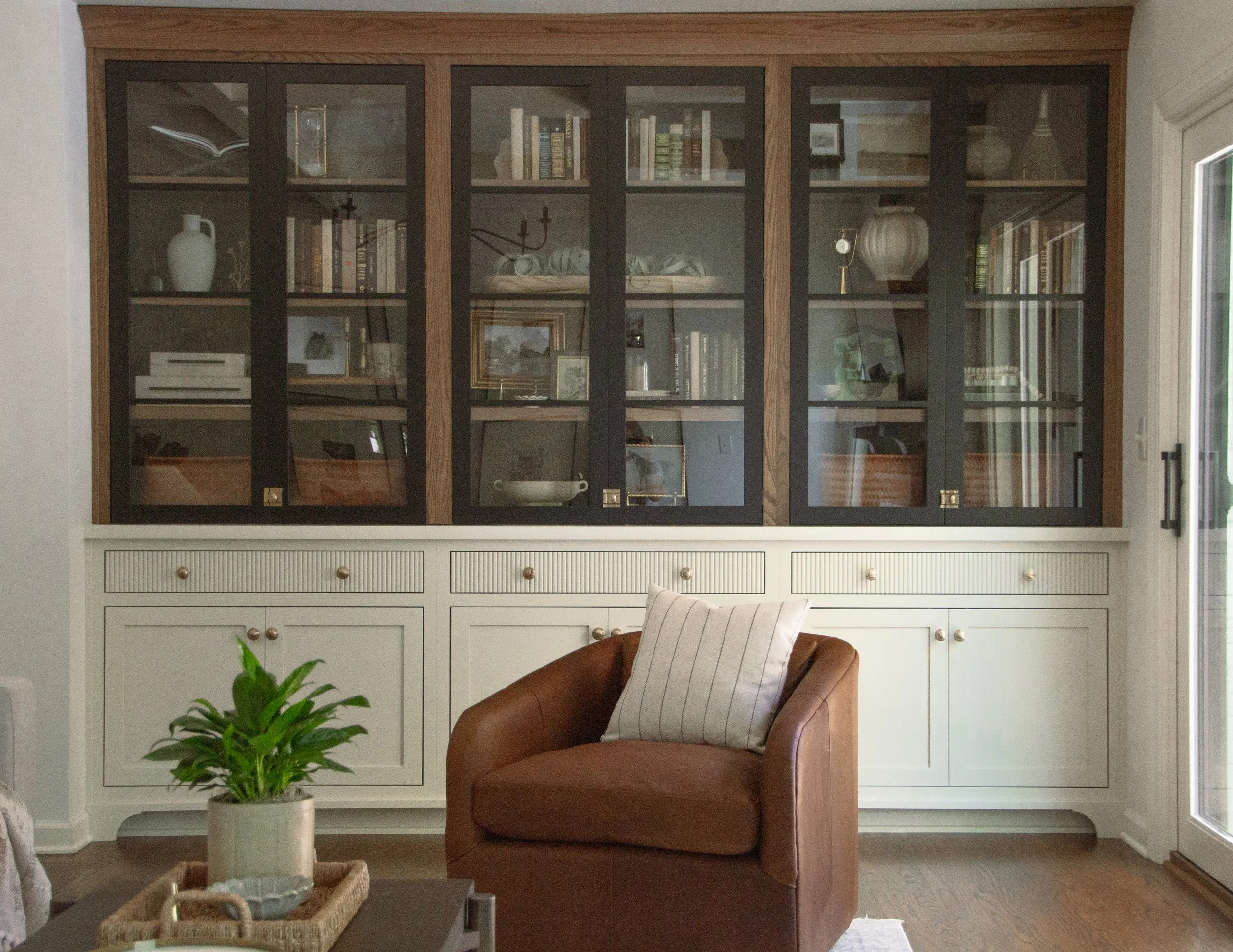 Custom built-in cabinetry with glass-front storage, wood detailing, and a leather accent chair in a thoughtfully designed living space.