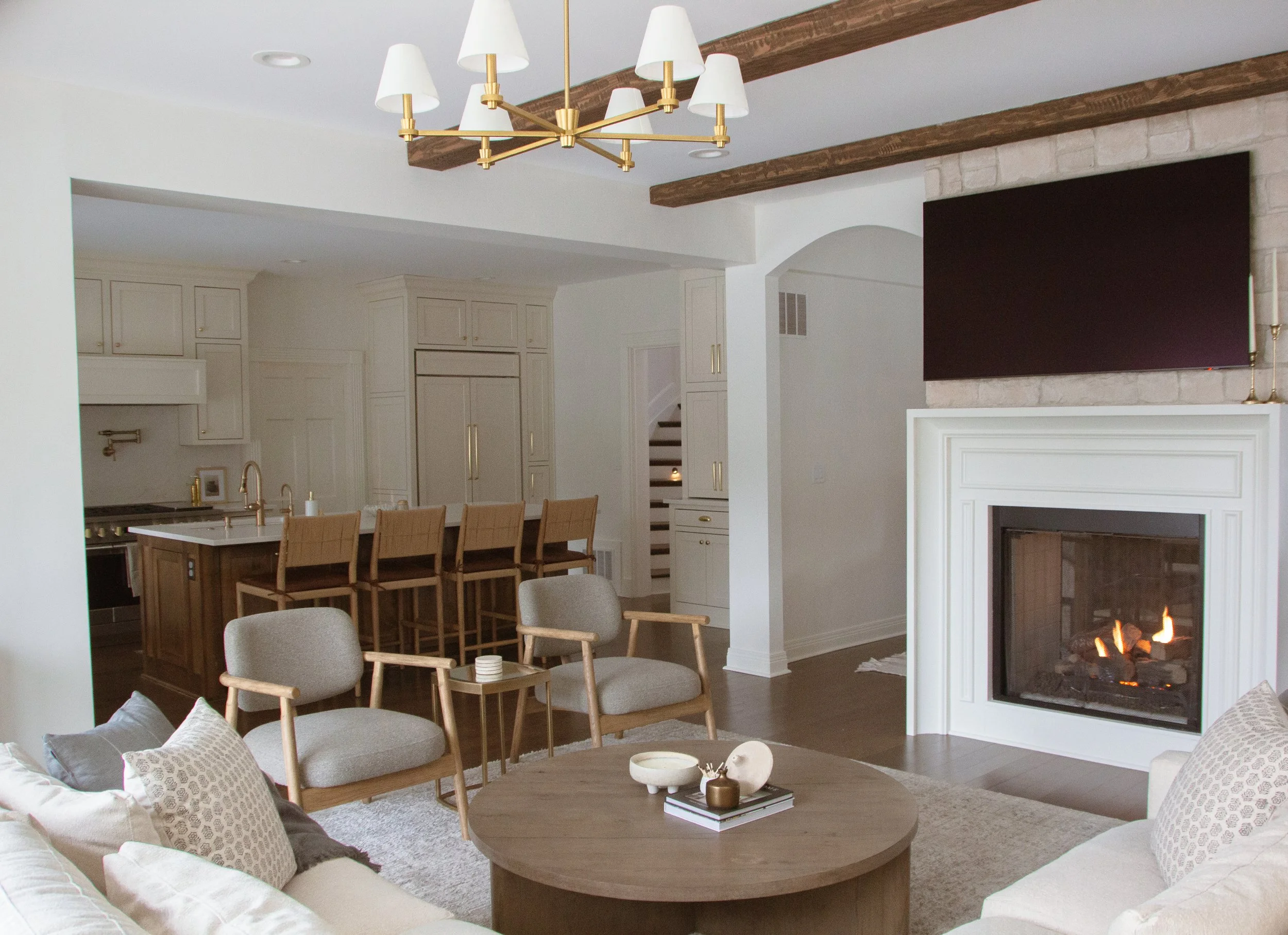 Open concept living room featuring a fireplace, round coffee table, accent chairs, and a kitchen with a large island and warm wood details.