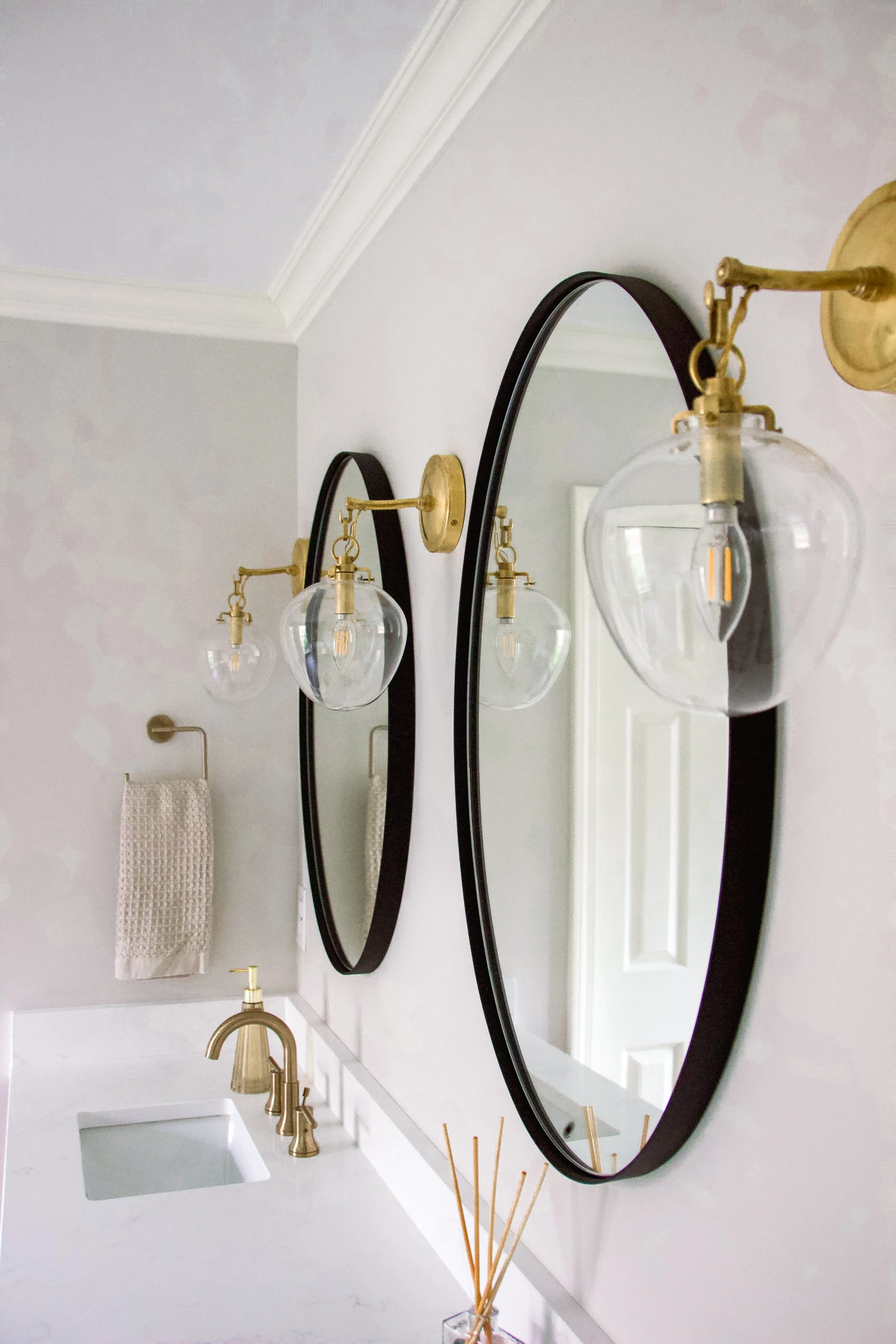 Oval mirrors with side-mounted glass sconces and warm metal fixtures providing even, flattering illumination at the vanity.
