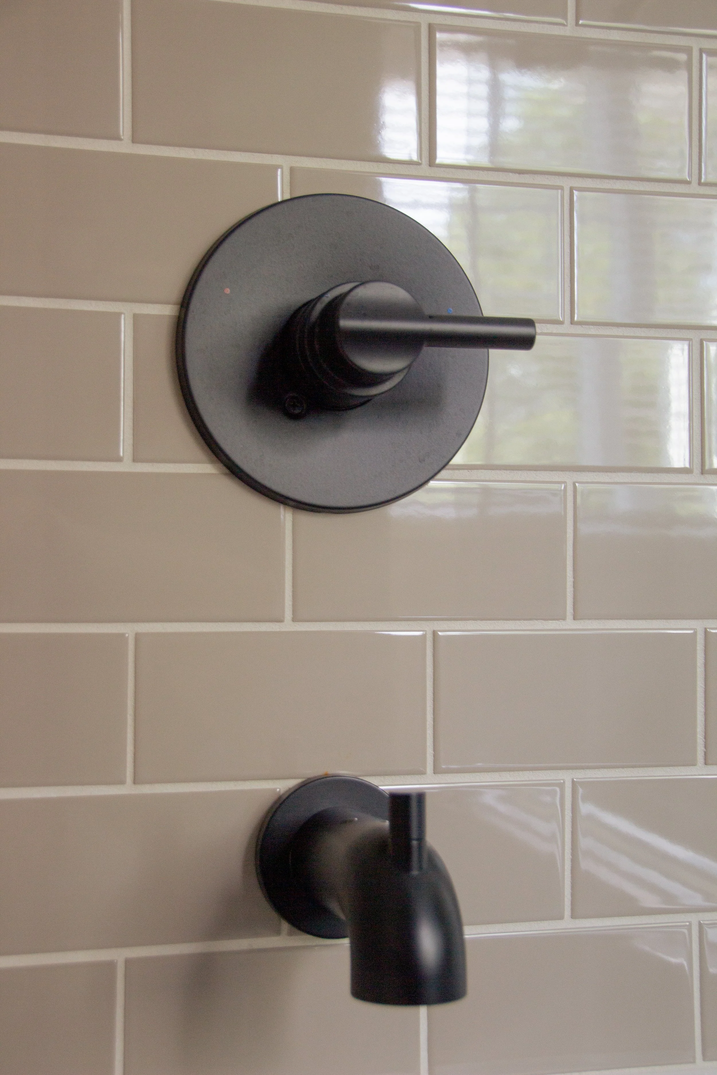 Matte black shower valve and tub spout set against glossy subway tile, emphasizing durable finishes and simple hardware placement.