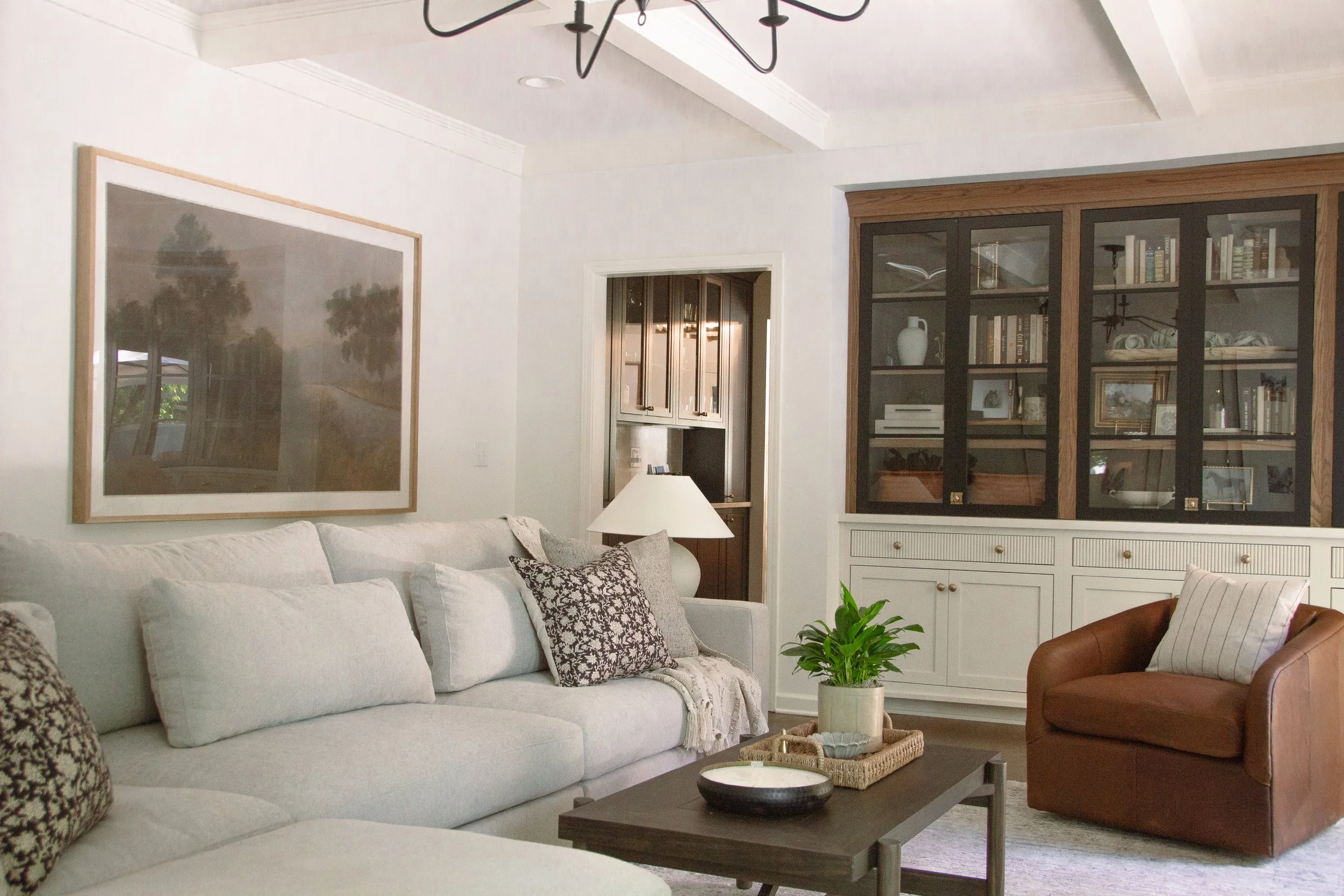 Living room featuring a light sectional sofa, leather accent chair, custom built-in cabinetry, and layered textures designed as part of a full-scale home renovation.