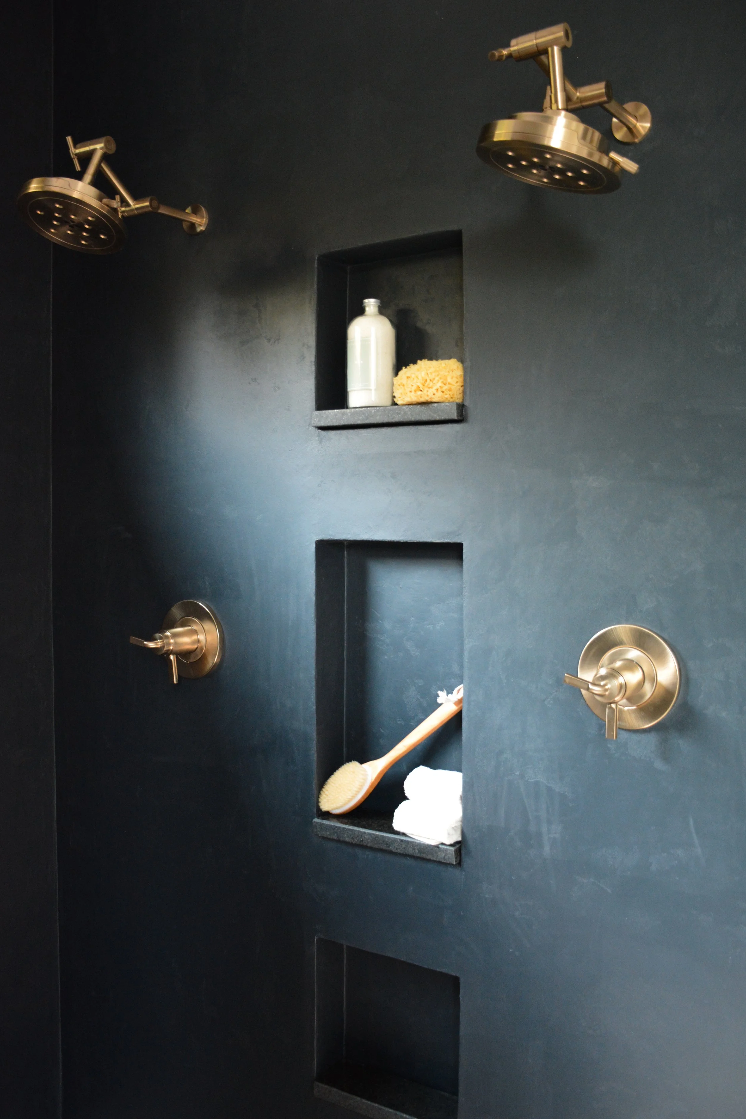 Matte dark shower walls with recessed niches and warm brass fixtures showing how metal finish choice changes contrast and longevity.