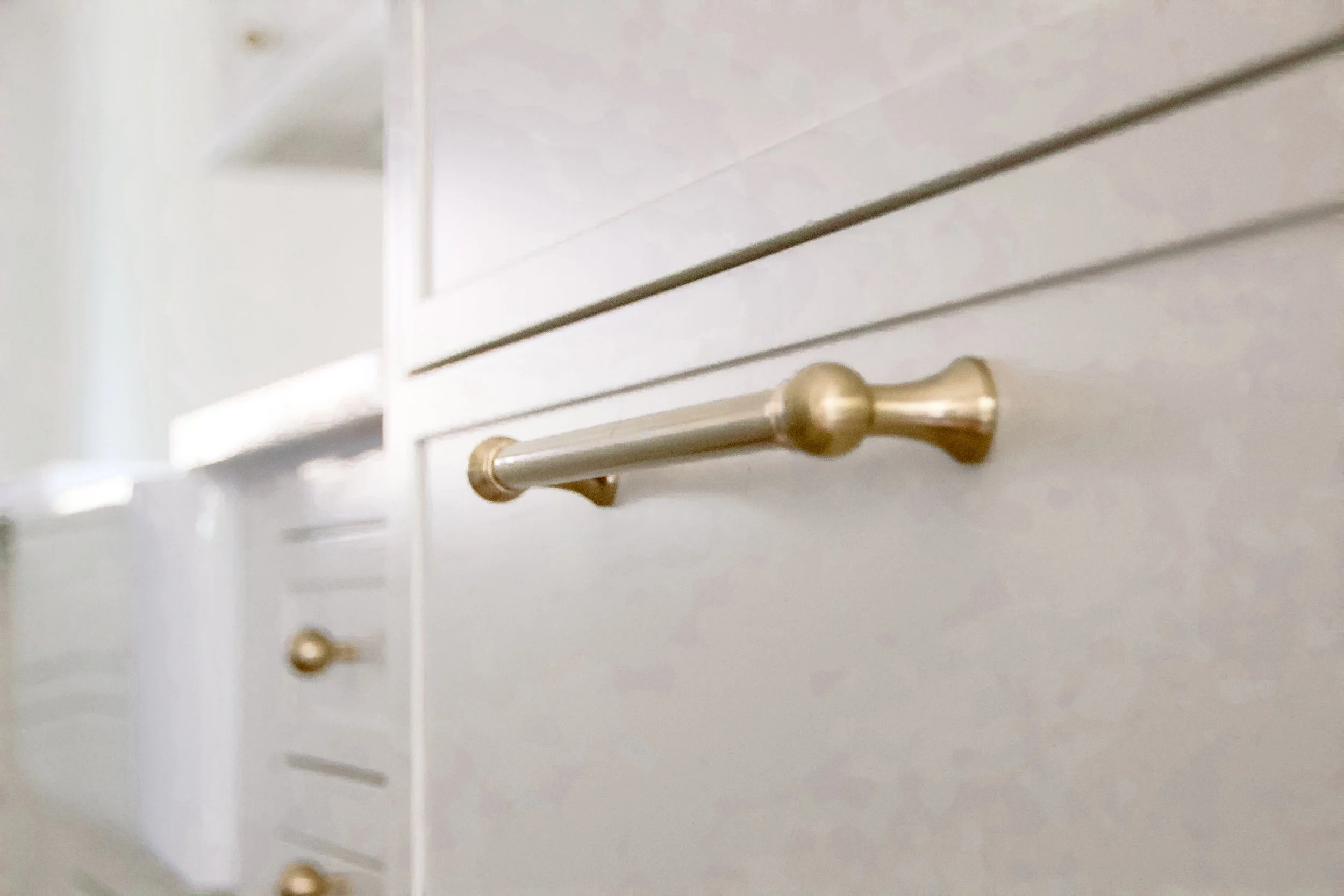 Brass drawer pull mounted on light cabinetry, showing consistent hardware selection and clean detailing across storage fronts.