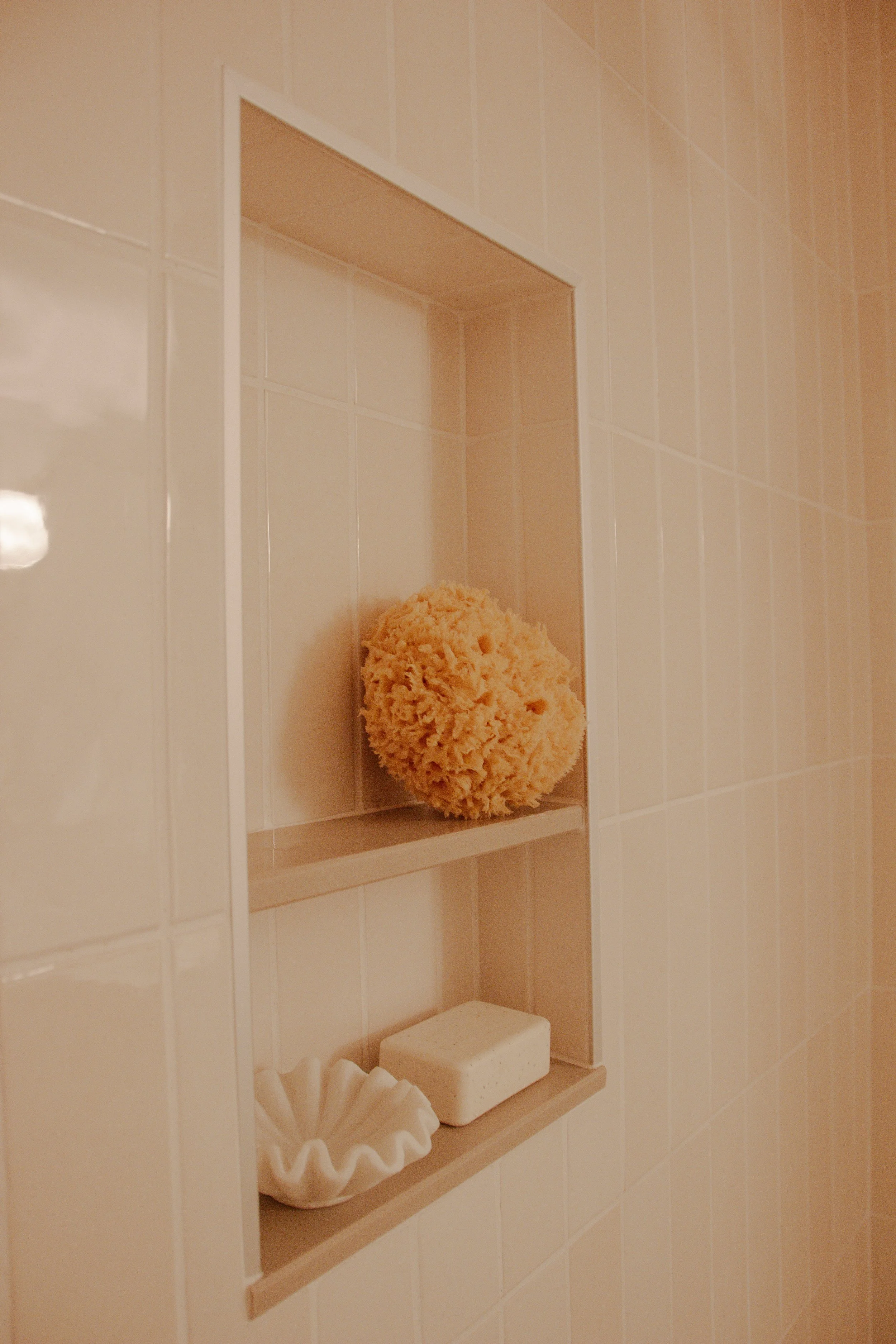 Recessed shower niche with vertically aligned shelves set into light tile, holding minimal bath accessories in a clean, proportional layout.