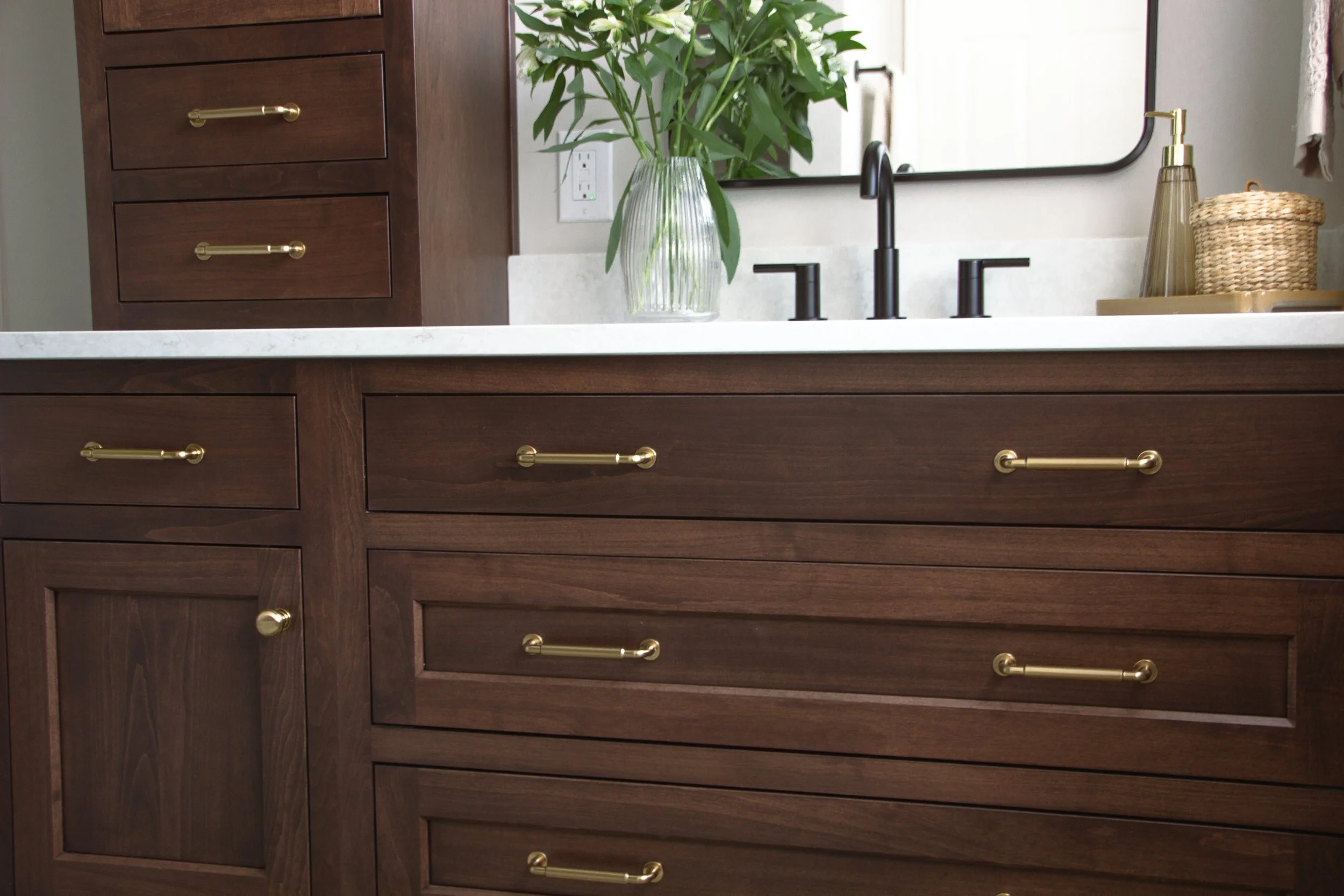 Dark wood vanity with brass pulls, a white countertop, and a matte black faucet highlighting clean-lined storage and an edited surface.