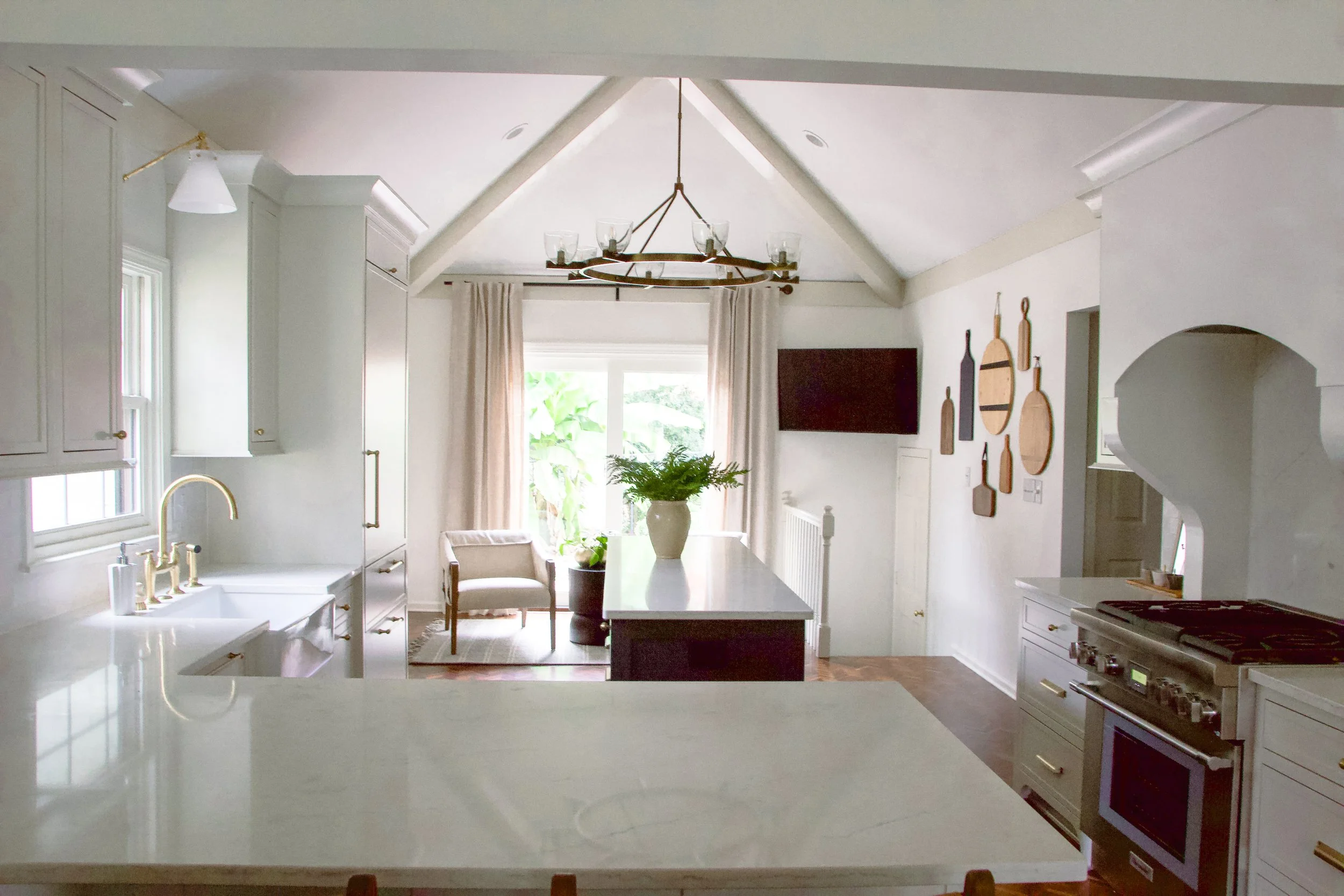 Transitional kitchen featuring a large island, vaulted ceiling, brass fixtures, custom cabinetry, and a connected seating area designed as part of a full-scale home renovation.