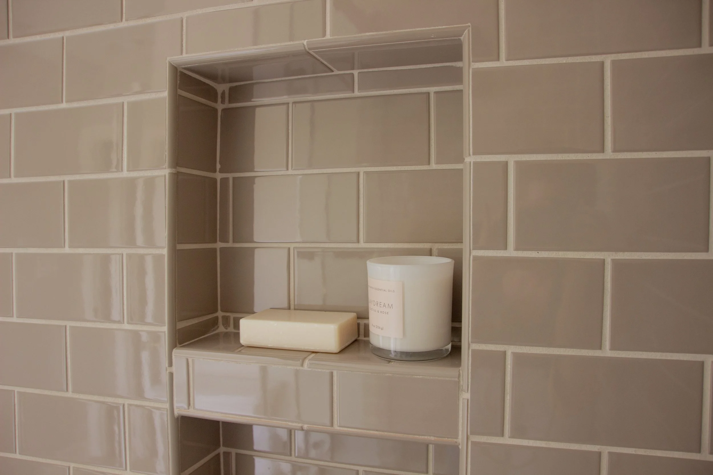 Recessed shower niche with glossy tile, integrated shelf, and minimal accessories showing clean grout lines and material continuity.