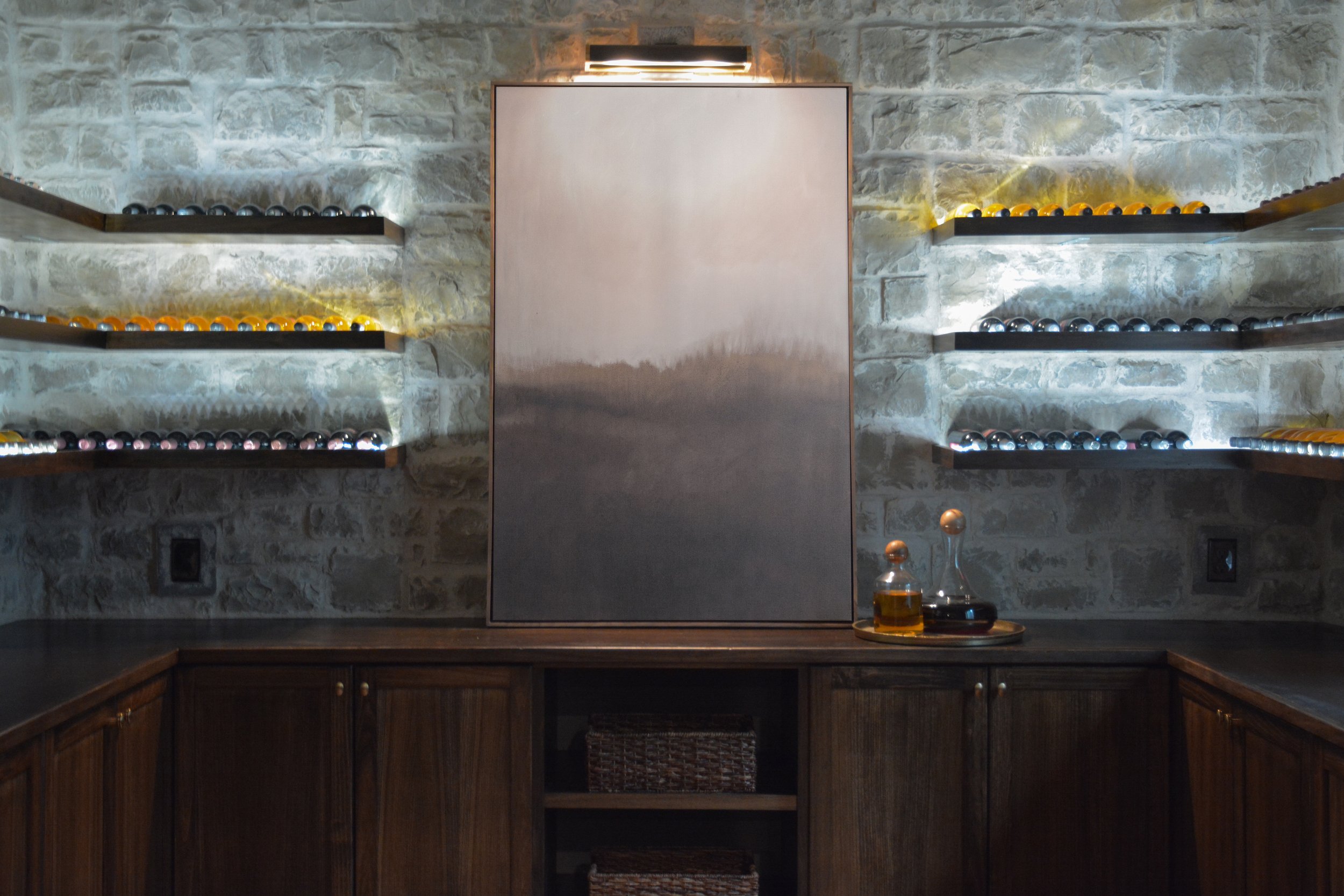 Basement wine display with stone accent wall, floating backlit shelves, and integrated wood cabinetry.