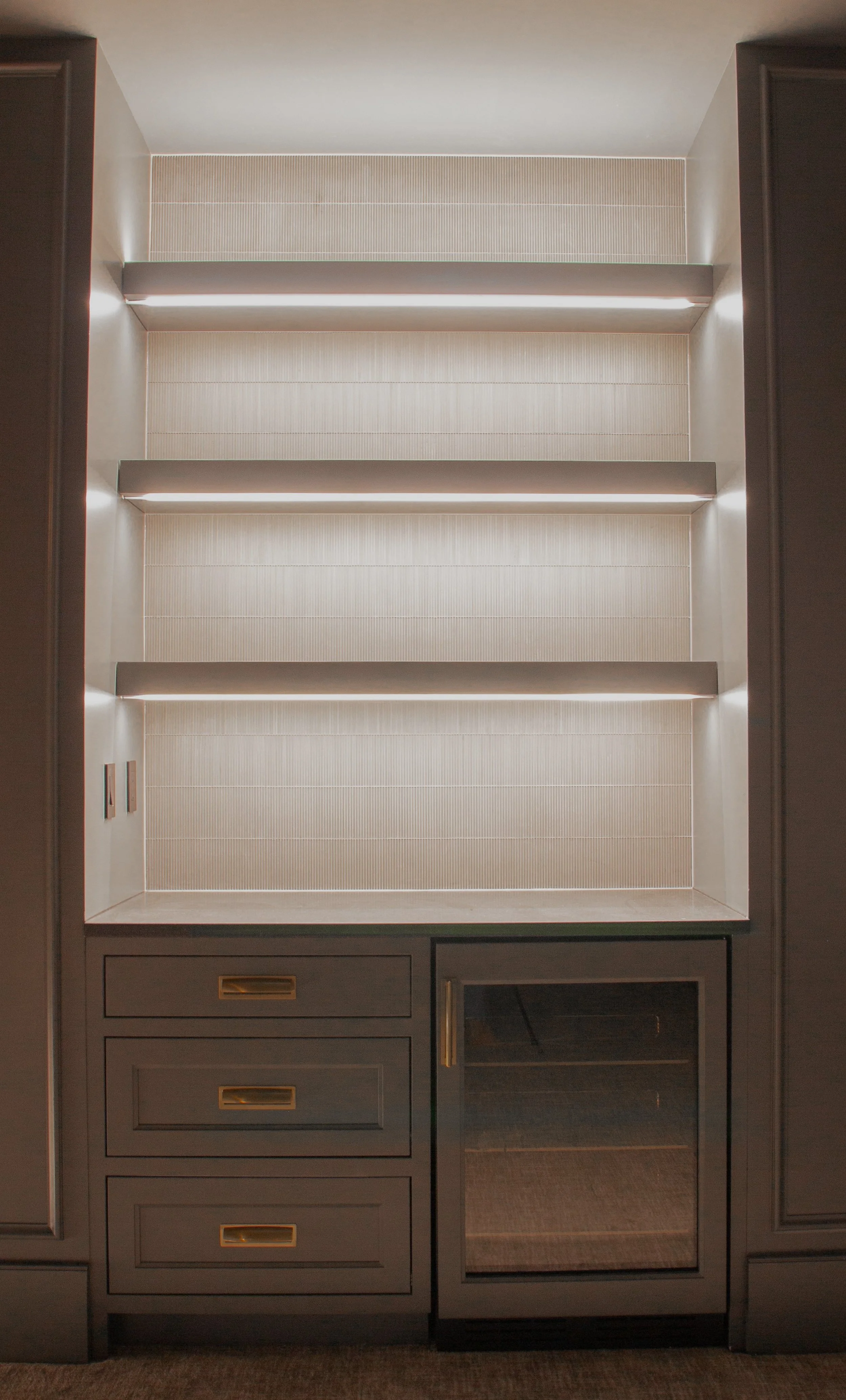 Custom beverage station featuring illuminated floating shelves, integrated drawers, glass-front refrigeration, and built-in cabinetry designed as part of a full-scale home renovation.