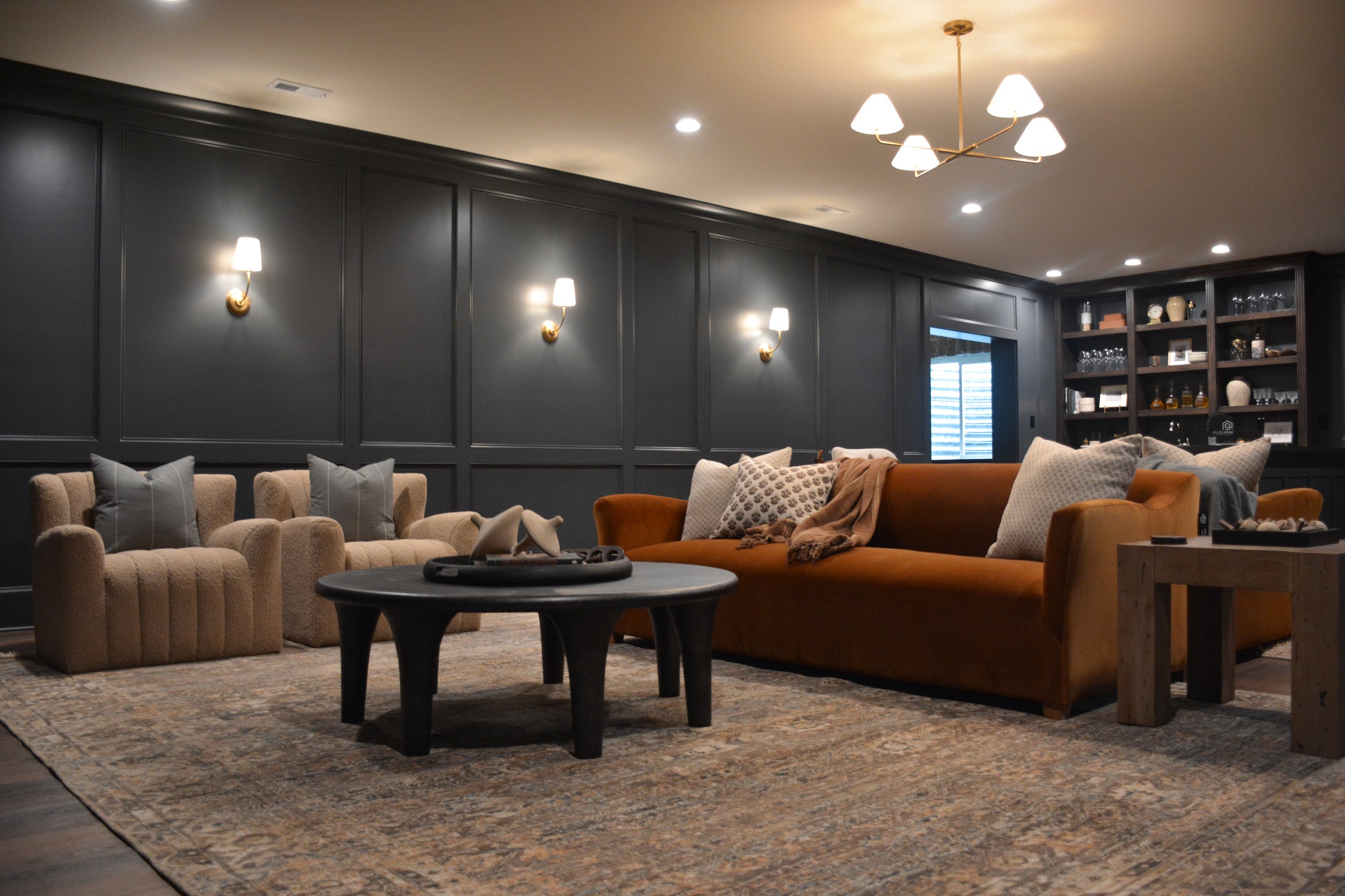 Modern Louisville basement lounge featuring a deep charcoal accent wall, warm layered lighting, and a large sectional arranged for comfortable lower-level gathering.