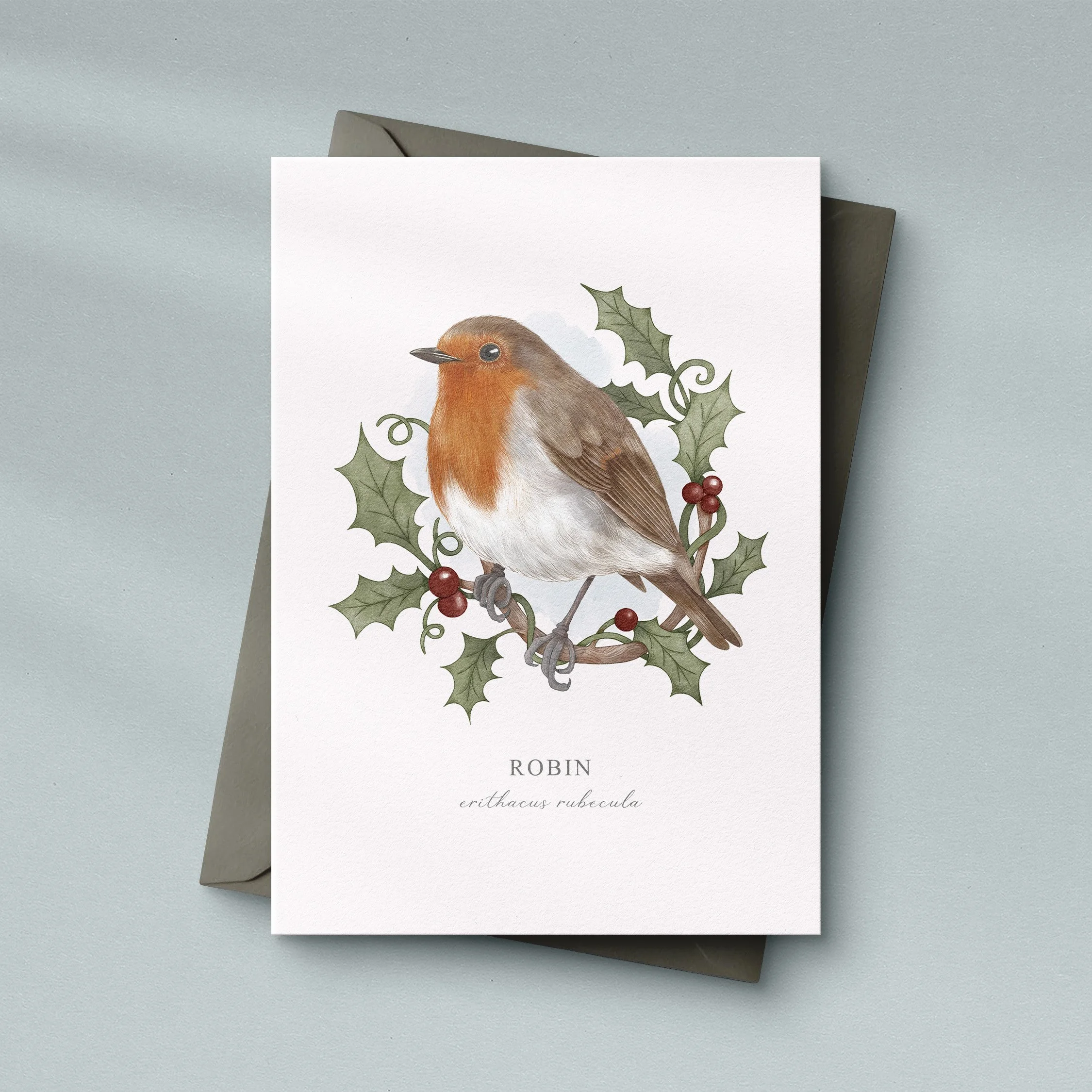Luxury robin watercolour greeting card sitting on a grey envelope. Designed by Cassandra Riley.