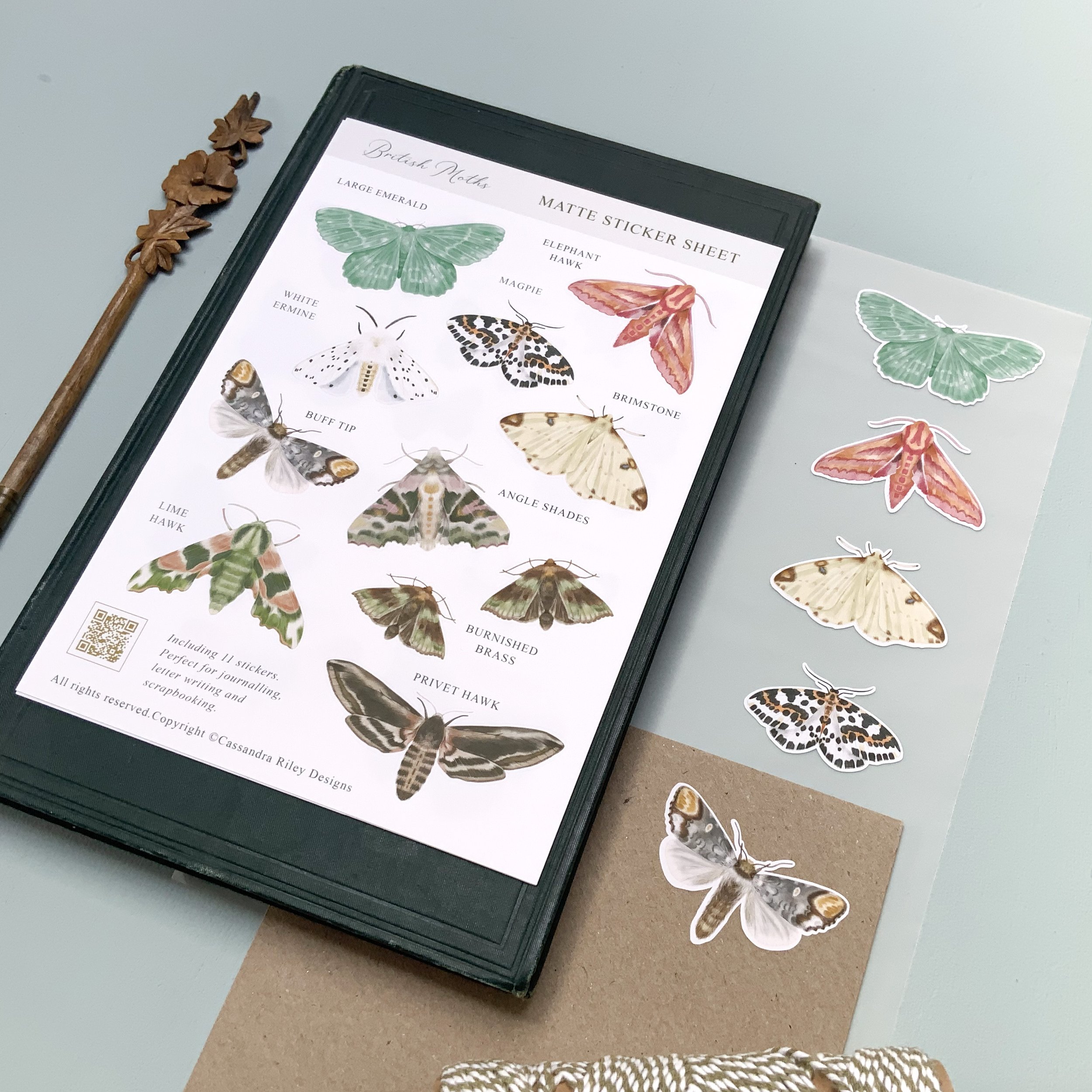 British Moth Sticker Sheet sitting on an antique book next to a wooden floral shaped antique dip pen.