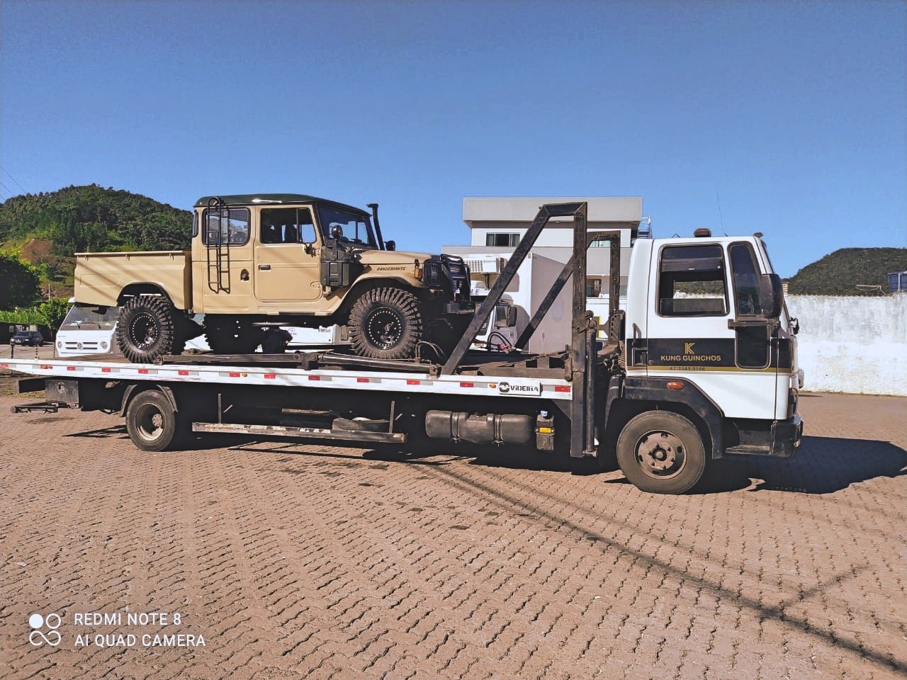 Tow truck carrying a beige off-road vehicle
