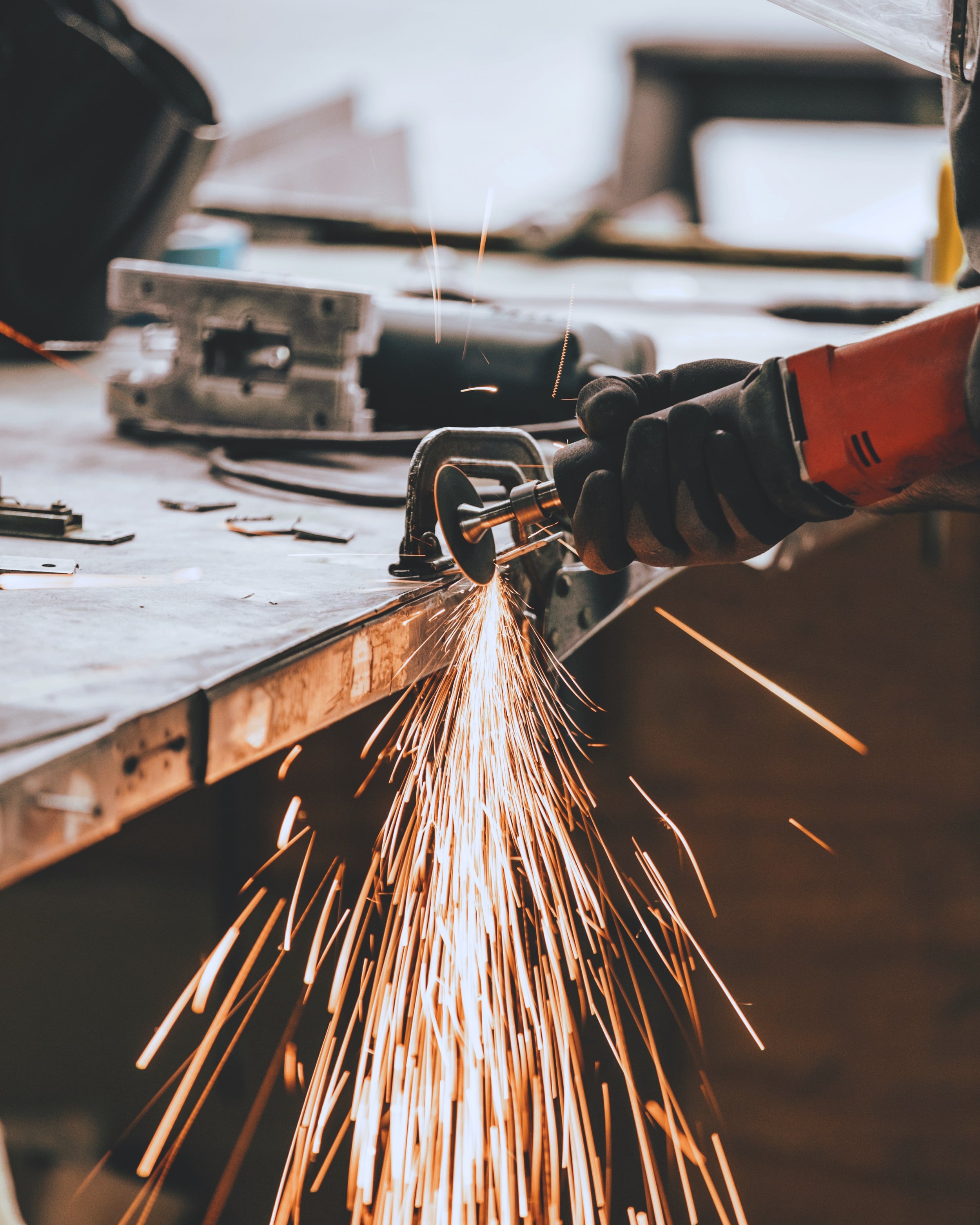 Person using an angle grinder, producing sparks, on a metal surface in a workshop.