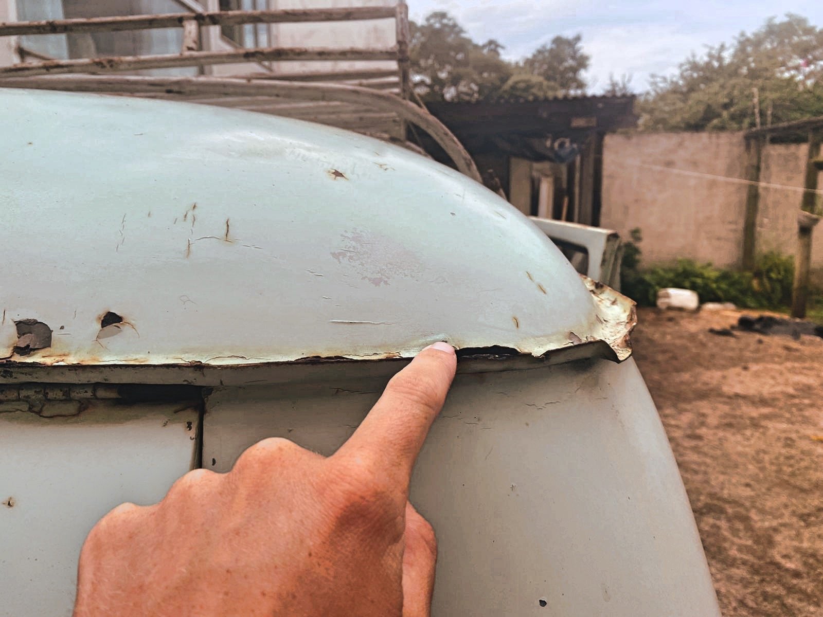 Close-up of a hand pointing to rusty, peeling metal on an old vehicle, showing signs of corrosion and damage.