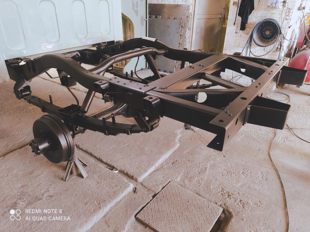 Vehicle frame in a workshop with suspension and axles, supported by stands.