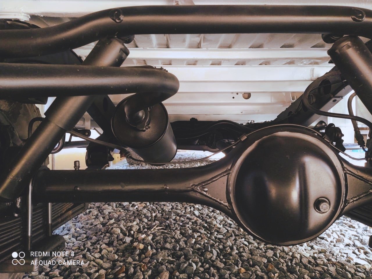 vehicle undercarriage showing suspension and differential with gravel beneath