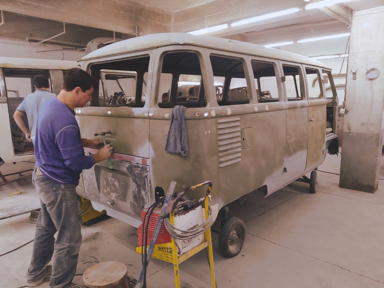 Two men working on restoring a vintage Volkswagen van in a garage.