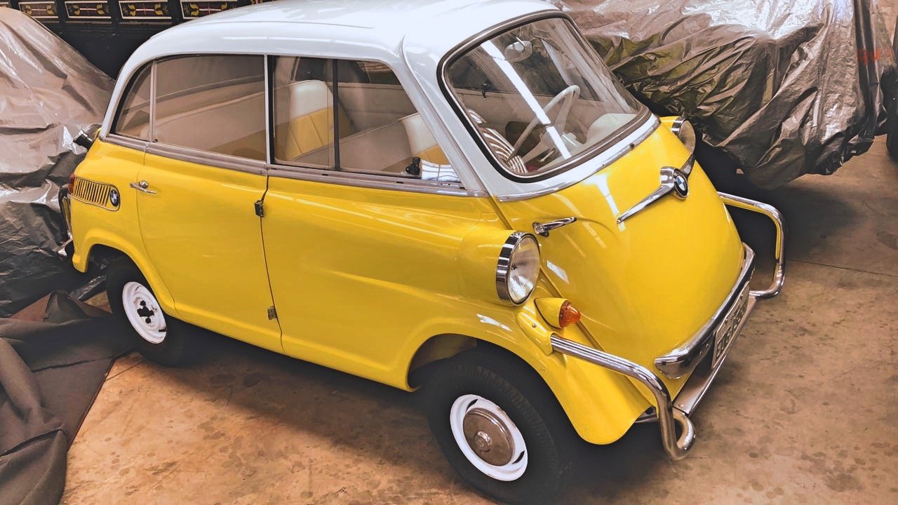 Yellow and white vintage BMW Isetta microcar in a garage with protective covers in the background.