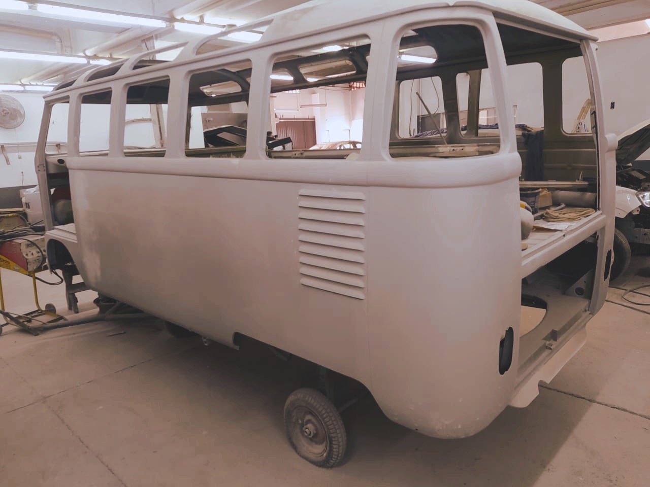 Volkswagen bus undergoing restoration in workshop; primed body, no windows, and interior exposed.