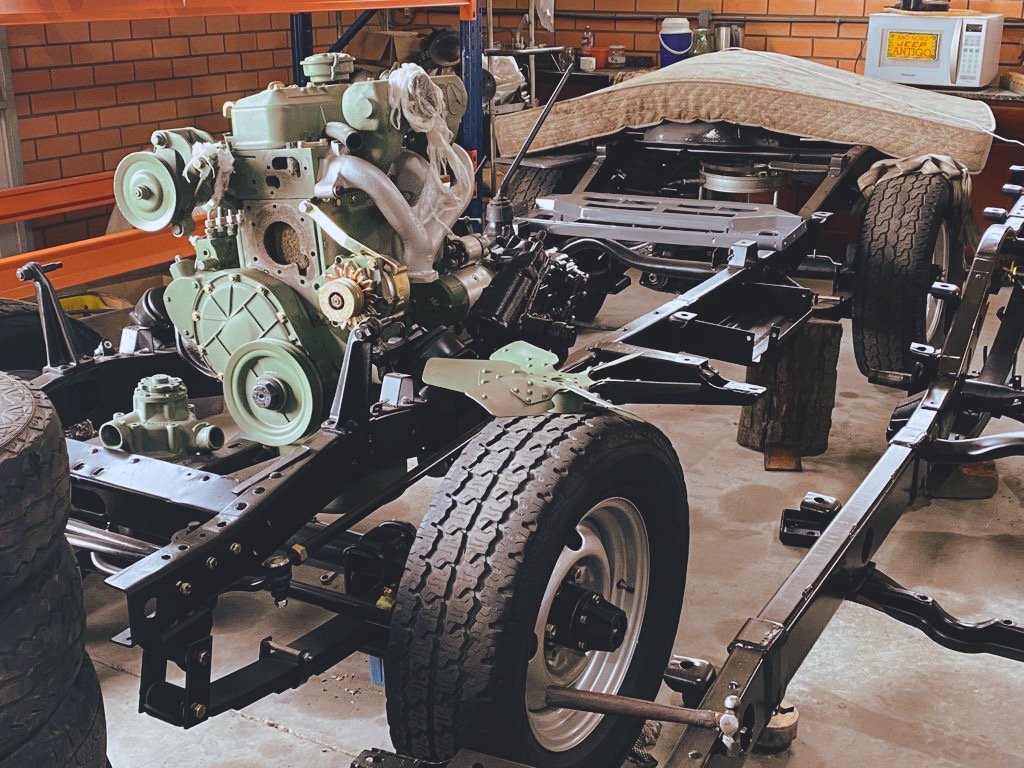 Vehicle chassis with mounted engine, exposed frame, and tires in a workshop setting.
