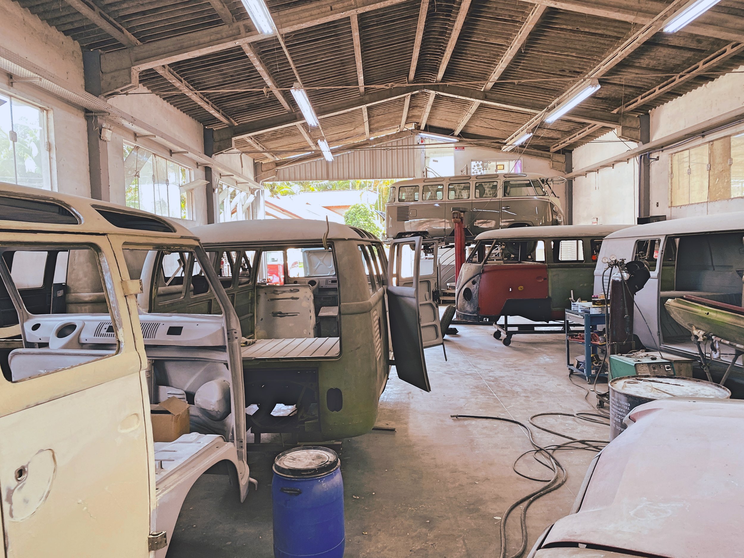 Interior of a workshop with several vintage Volkswagen vans in various stages of restoration.