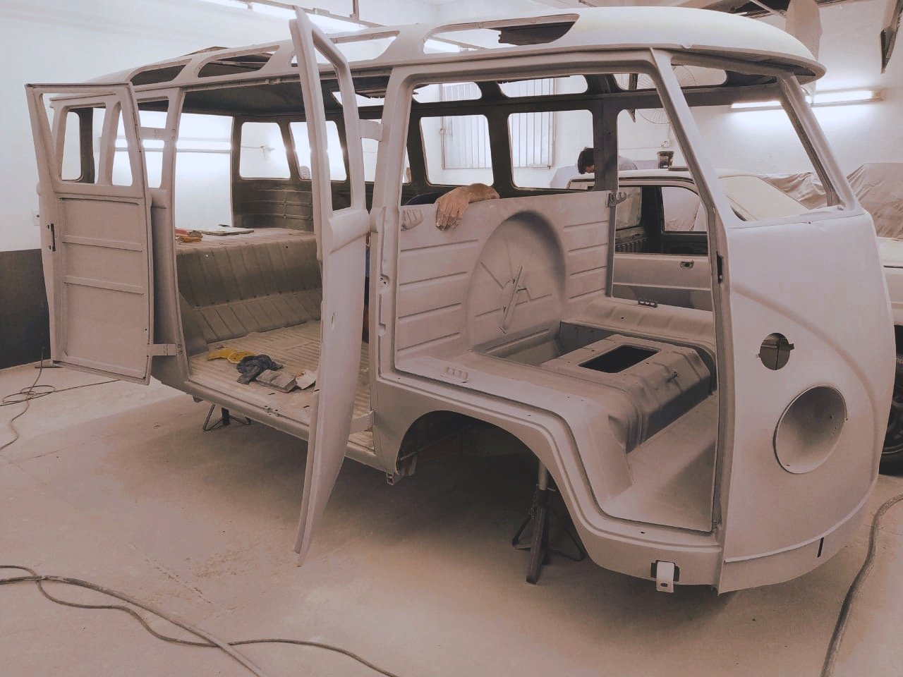 Unpainted vintage van shell in garage, rear view.