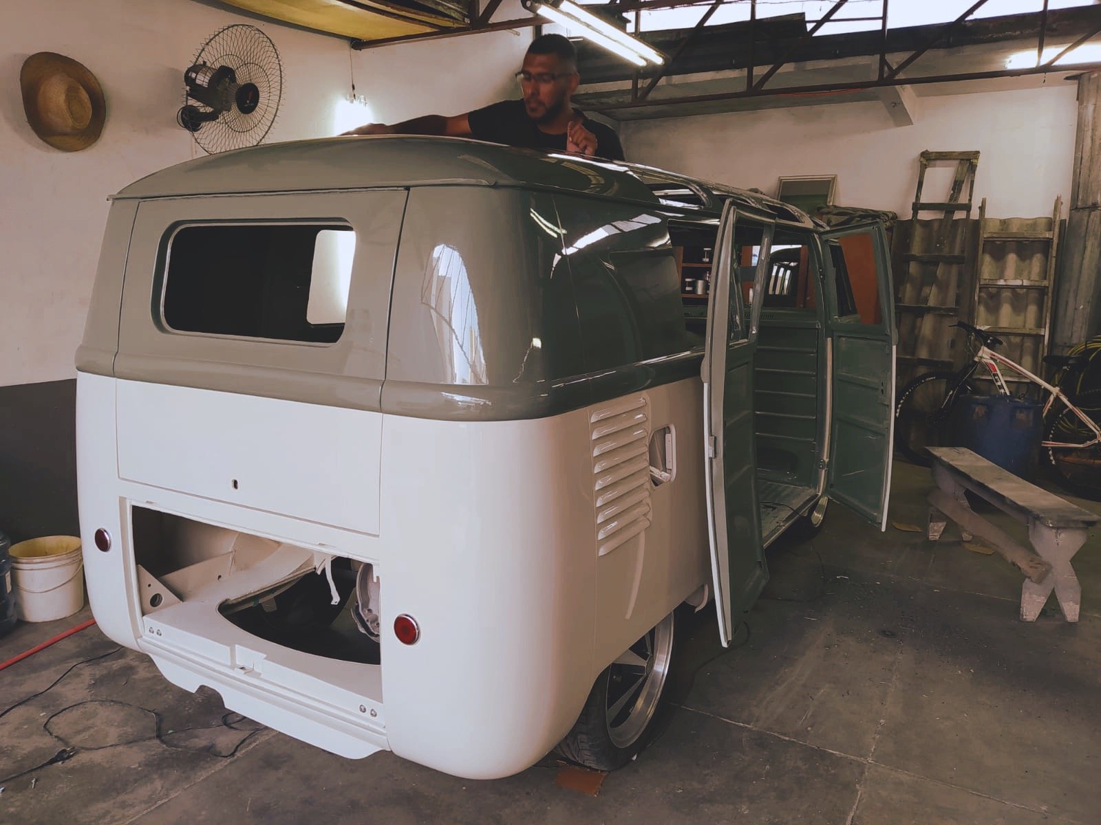 Vintage VW van restoration in a garage workshop, partially painted with open doors and exposed rear.