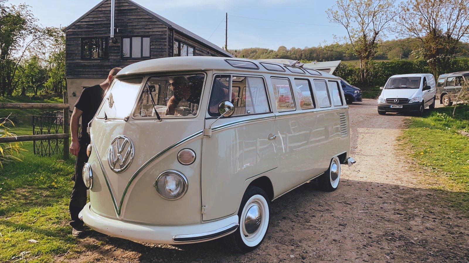 Vintage Volkswagen camper van parked near a house with trees in the background.