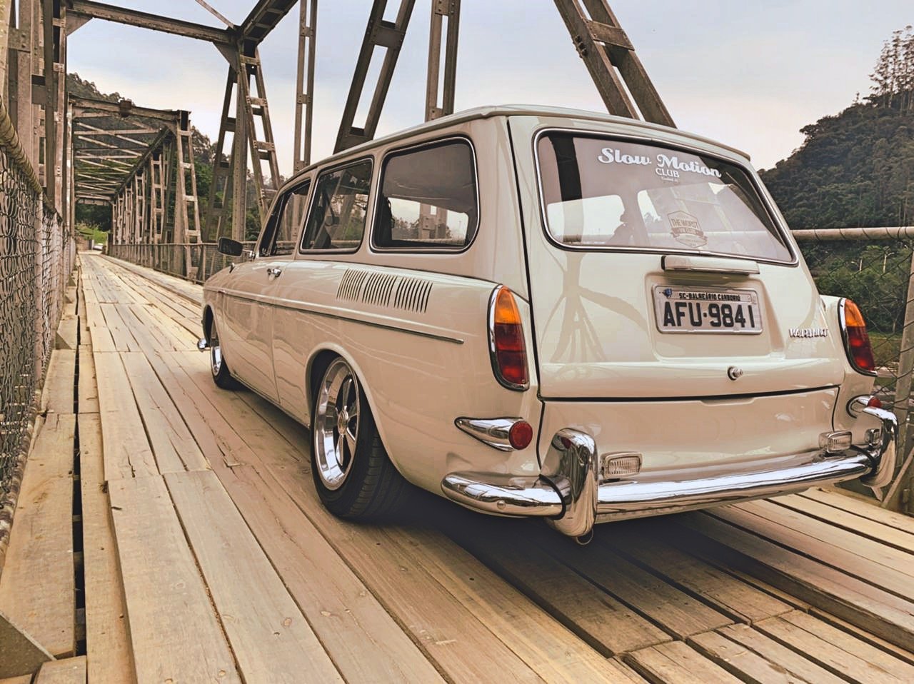 Vintage Volkswagen Variant car on a wooden bridge with metal supports, forest background.
