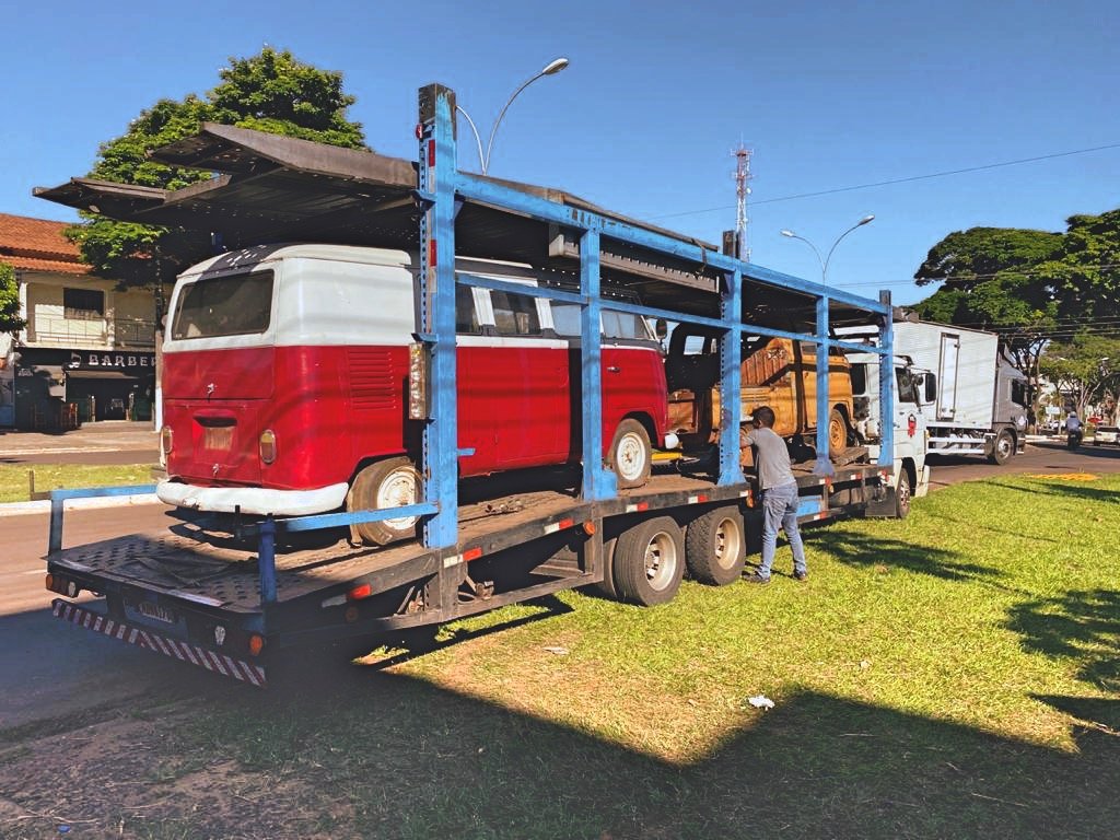 Two vintage Volkswagen vans on a car transport trailer with a person nearby.