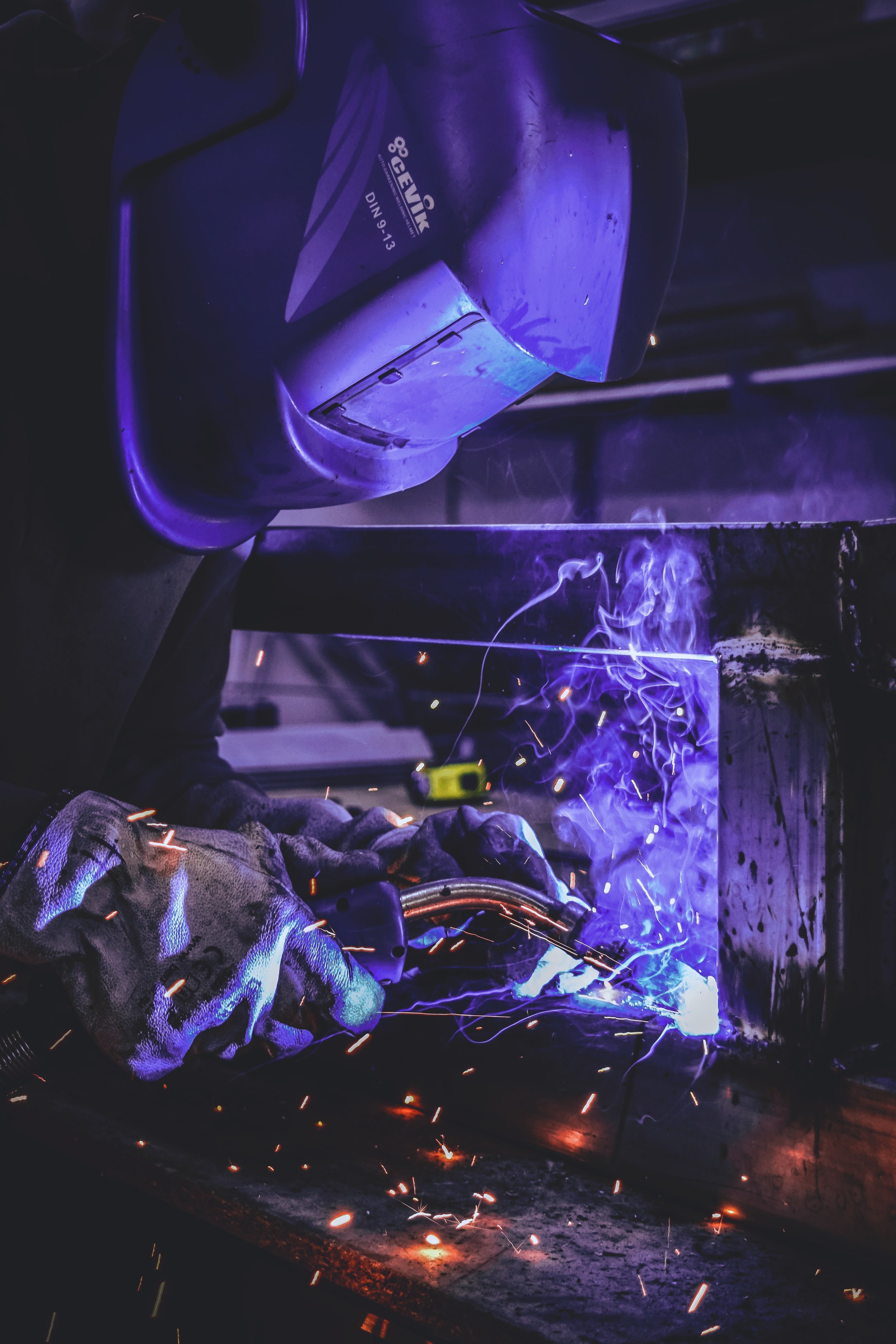 Welder wearing a helmet and gloves working with sparks and smoke.
