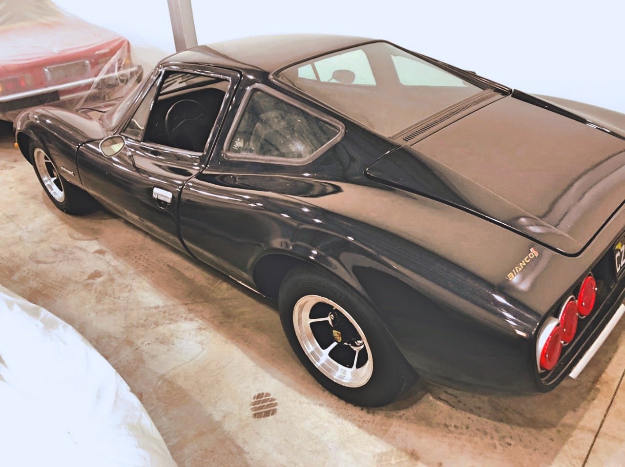Black sports car in storage with red three-taillight design and classic styling.