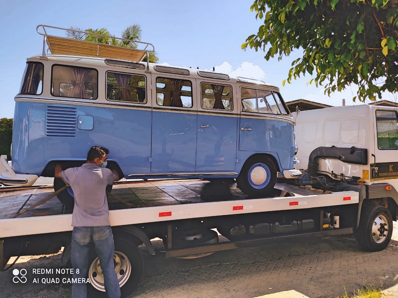 Blue vintage Volkswagen van on a flatbed truck with a person securing it.