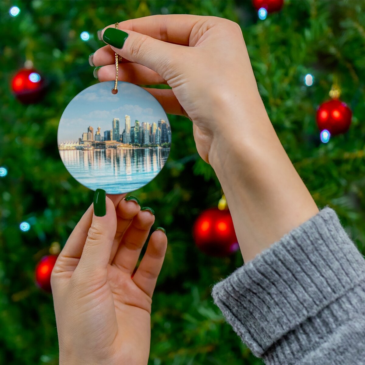 Lady elegantly hanging a double-sided Vancouver-themed porcelain ornament on a Christmas tree, adding a touch of urban and coastal charm to holiday décor.